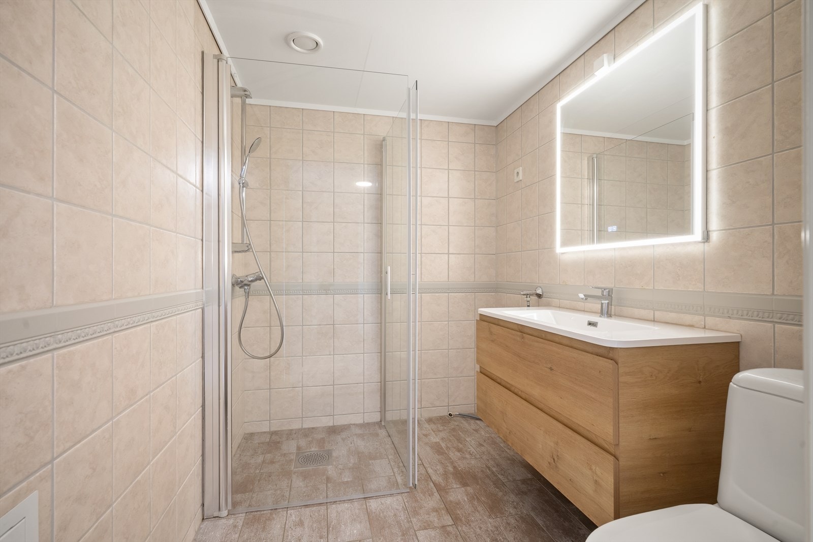 Badet har flislagte vegger og gulv med elektriske varmekabler og dusjvegger med veggmontert armatur. Galleribilde