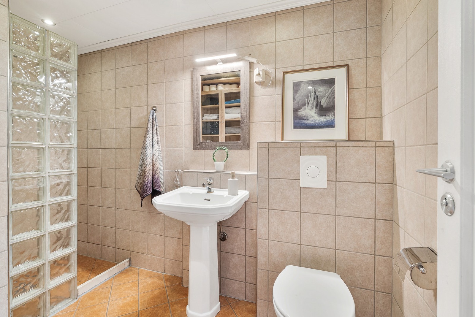 Badet i andre etasje har flislagt gulv med varmekabler, veggmontert toalett, servant og dusjhjørne. Galleribilde