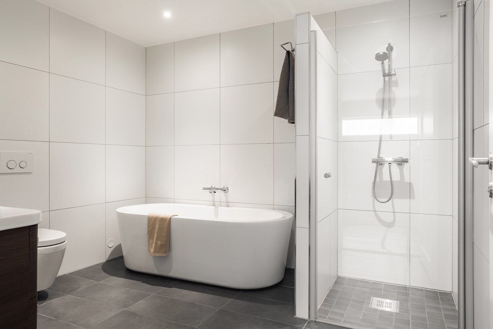 Badet har keramiske fliser på gulv og vegger samt malte flater i himling. Dusjnisjen er utstyrt med fastvegg og innfellbare dører i herdet glass. Galleribilde