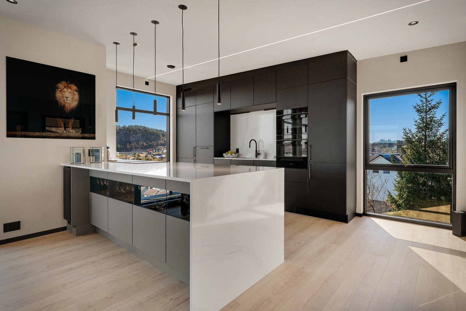 Kjøkkenet fra 2025 har en stor øy og rikelig med skapplass. Elegant steinbenkeplate med gjennomført bruk av samme materiale ved vask og som stilren backsplash. Galleribilde