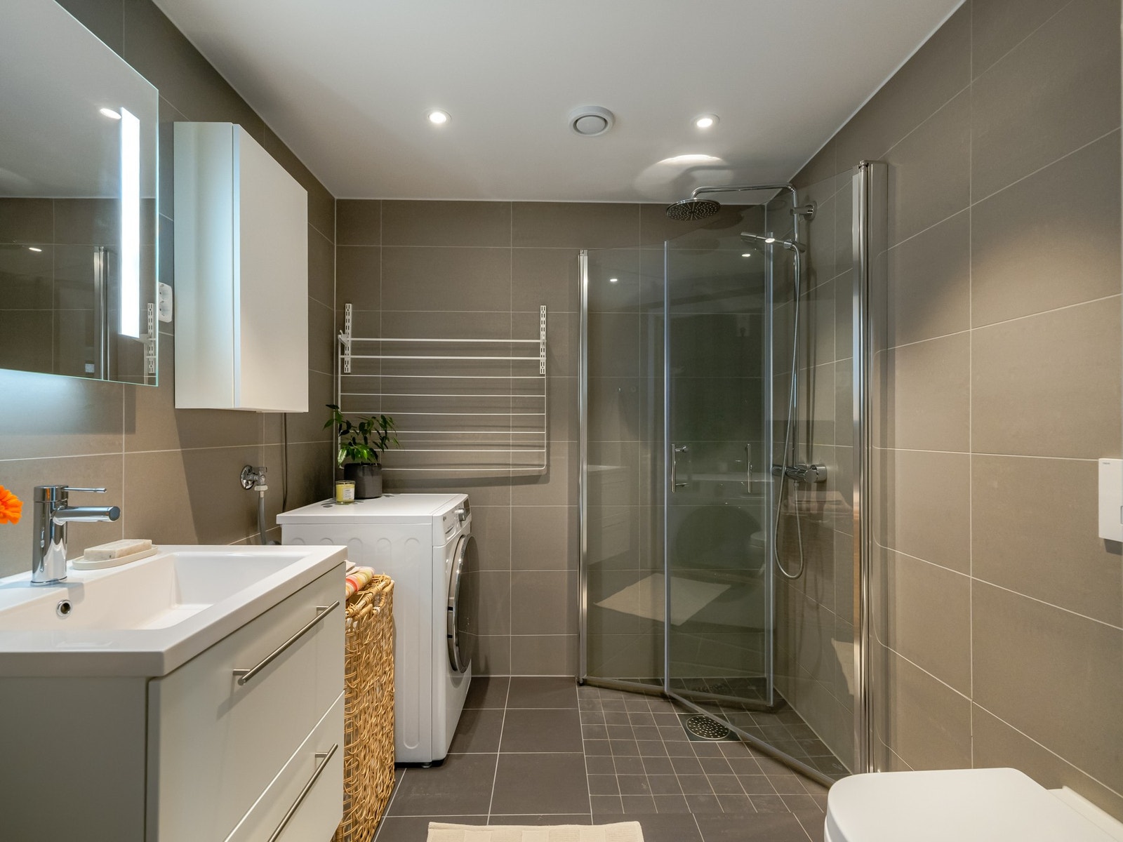 Det er plass til både vaskemaskin og tørketrommel. Badet er innredet med servantskap med skuffer, dusjsone med innfellbare glassdører og vegghengt toalett. Galleribilde