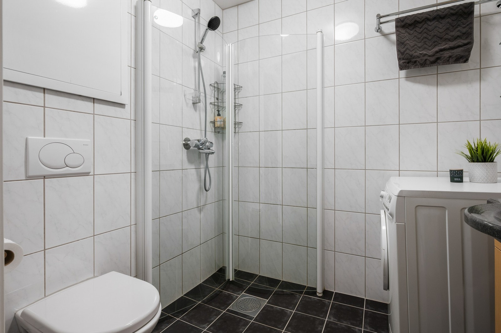 Badet er utstyrt med vegghengt toalett, dusjhjørne, servantskap og opplegg for vaskemaskin Galleribilde