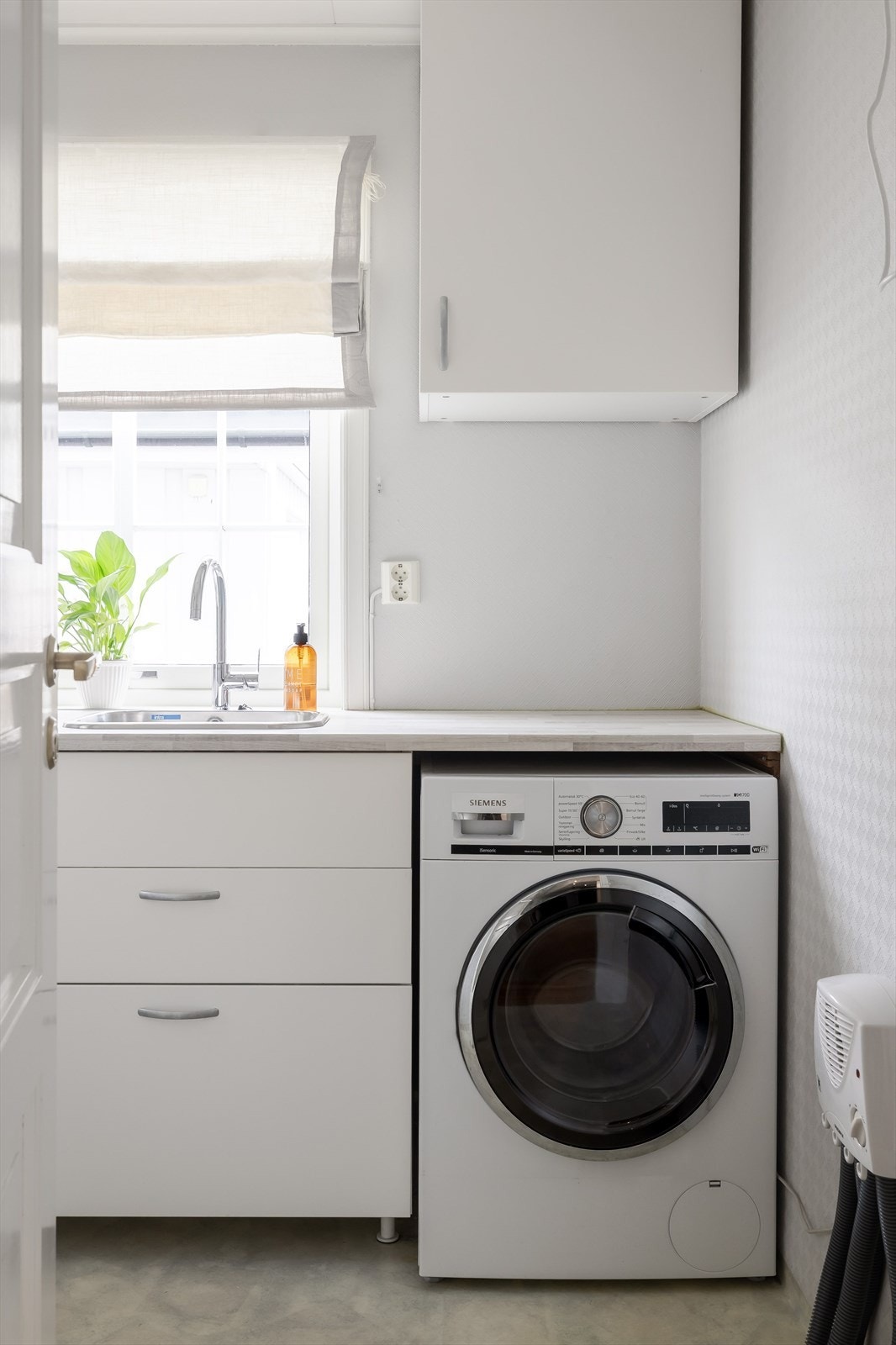 Boligen har også et lyst og praktisk vaskerom i 1. etasje. Vaskeromsinnredning fra 2017 med hvite glatte fronter og laminert benkeplate med nedfelt kum. Praktisk med plass og opplegg for vaskemaskin under benkeplaten. Galleribilde