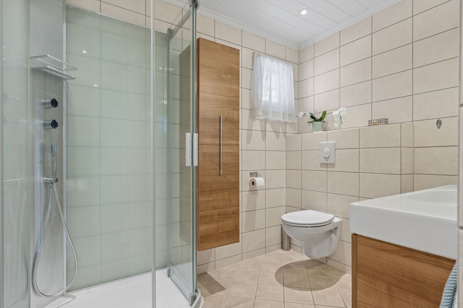 Badet er utstyrt med vegghengt toalett, servant med innredning og dusjkabinett. Galleribilde