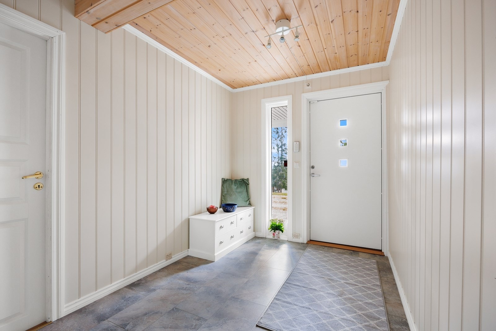 Entréen er lys og tiltalende med grått flislaminat på gulvet og lysmalte panelvegger. Galleribilde