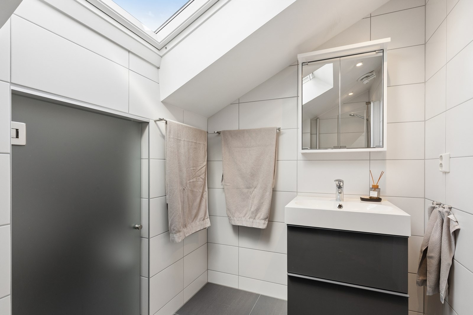 Badet er innredet med vegghengt toalett, dusjhjørne og en servant med underskap. Tilgang til bod via dør i bildet. Galleribilde