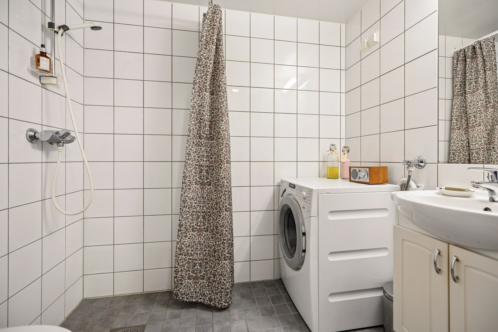 Praktisk baderomsinnredning med benkeskap og veggskap med profilerte fronter, samt innfliset speil over servant og opplegg for vaskemaskin. Galleribilde