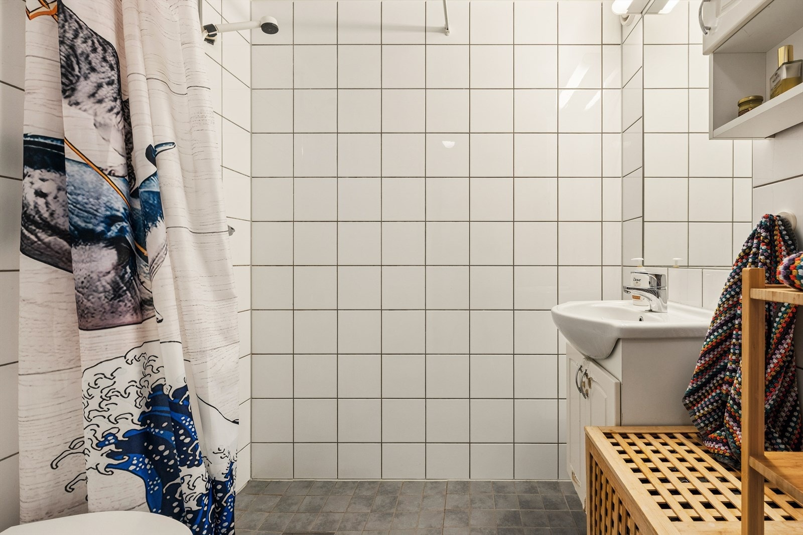Bad i hybeldelen med flislagte vegger og gulv med gulvvarme. Rommet har dusjløsning på gulv, veggfestet klosett med innebygget sisterne og servant. Baderomsinnredning med benkeskap og veggskap med profilerte fronter samt innfliset speil over servant. Galleribilde