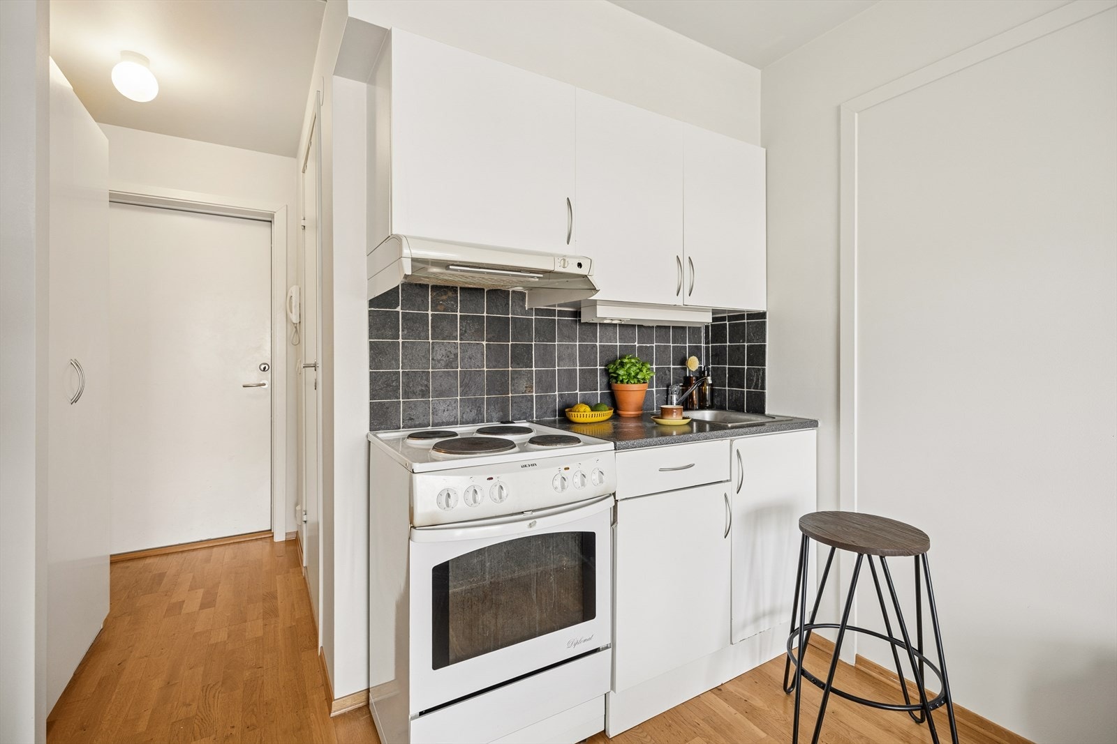 Kjøkkeninnredning med glatte fronter og laminat benkeplate med nedfelt kum i rustfritt stål. Fliser over benkeskap samt belysning under overskap. Galleribilde