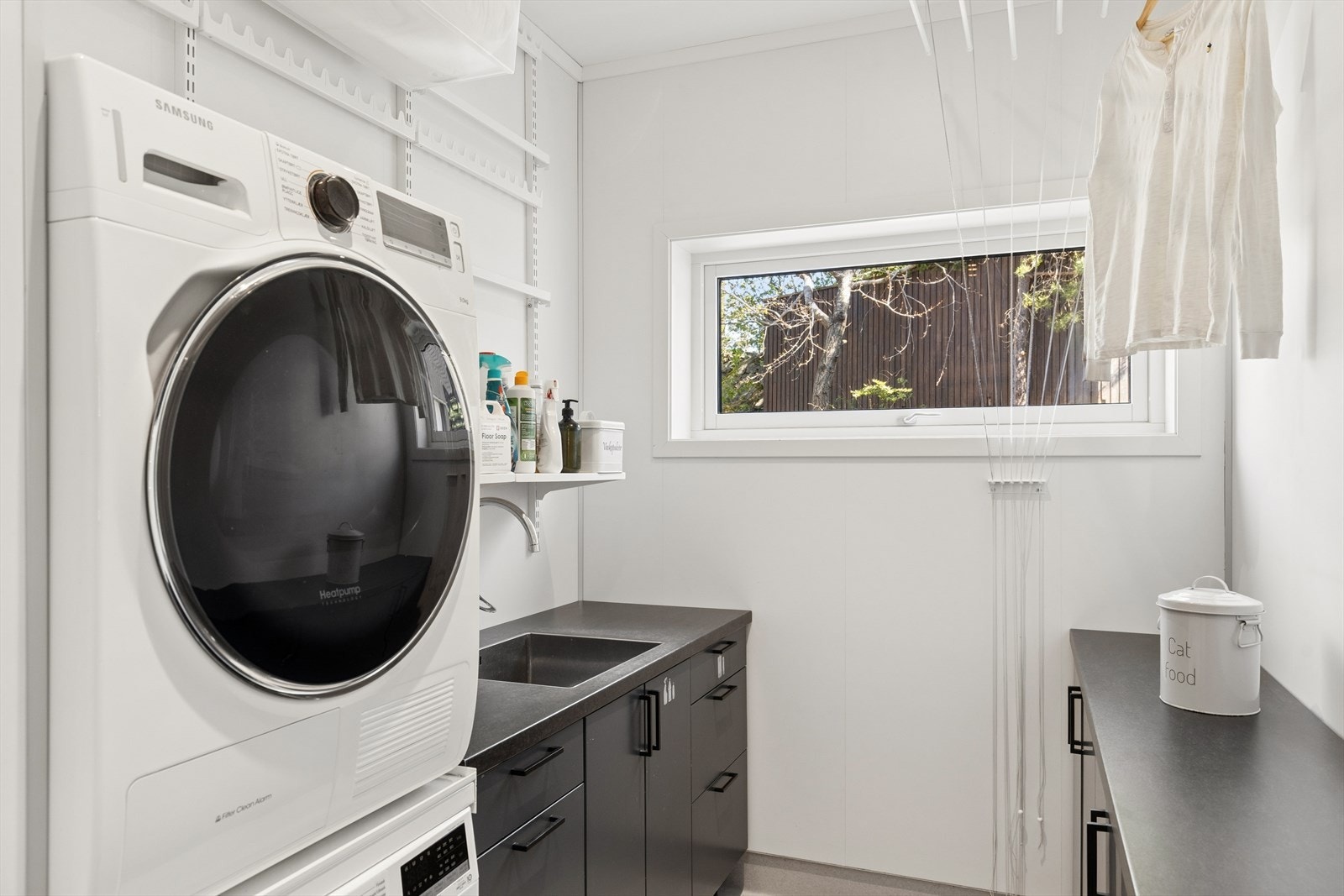 Et praktisk vaskerom med egen utgang til hagen, innredet med benkeskap, skyllekum og opplegg for vaskemaskin. Galleribilde