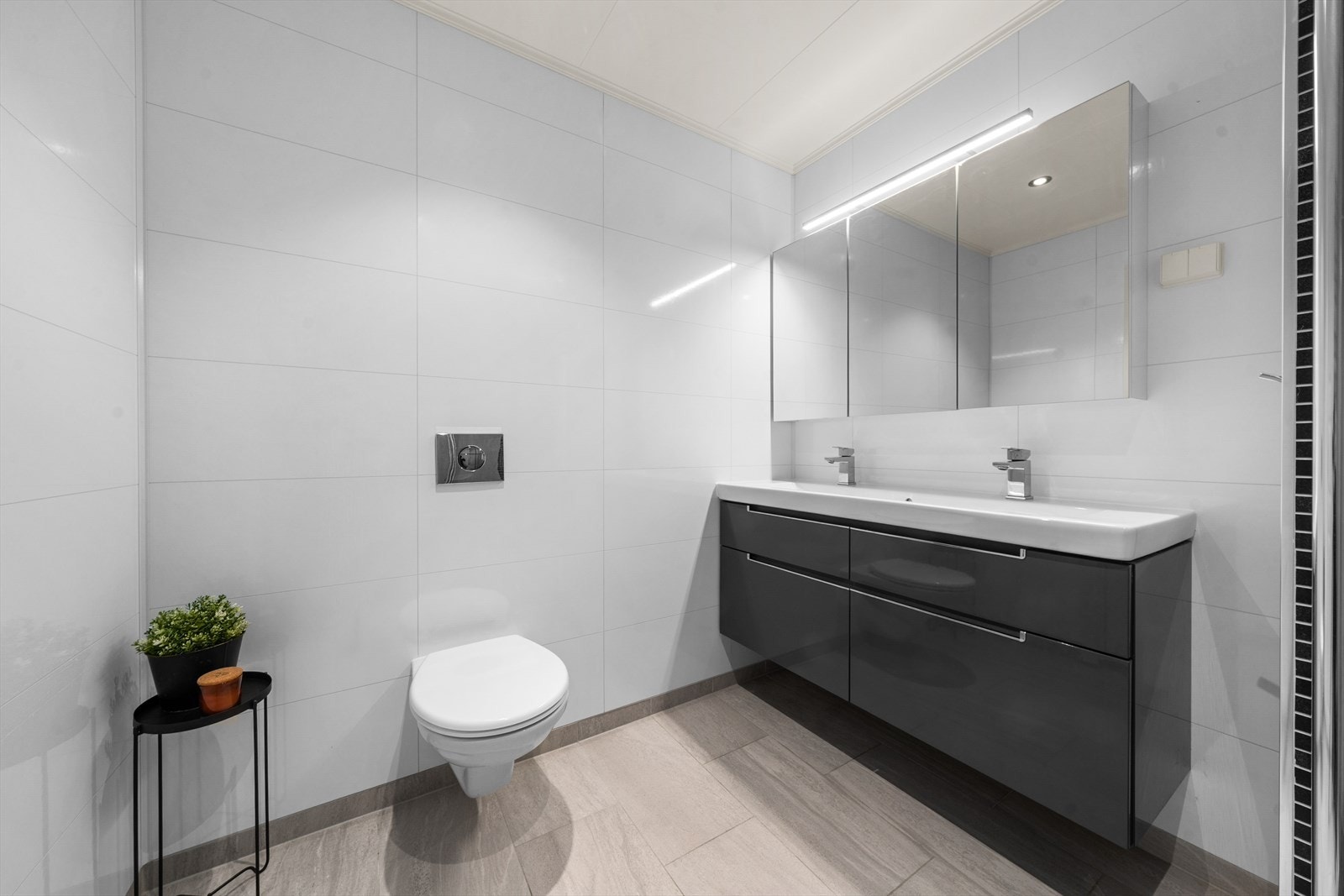 Badet er utstyrt med servantskap med mørke/glatte fronter, toalett og dusjhjørne med dører. Galleribilde