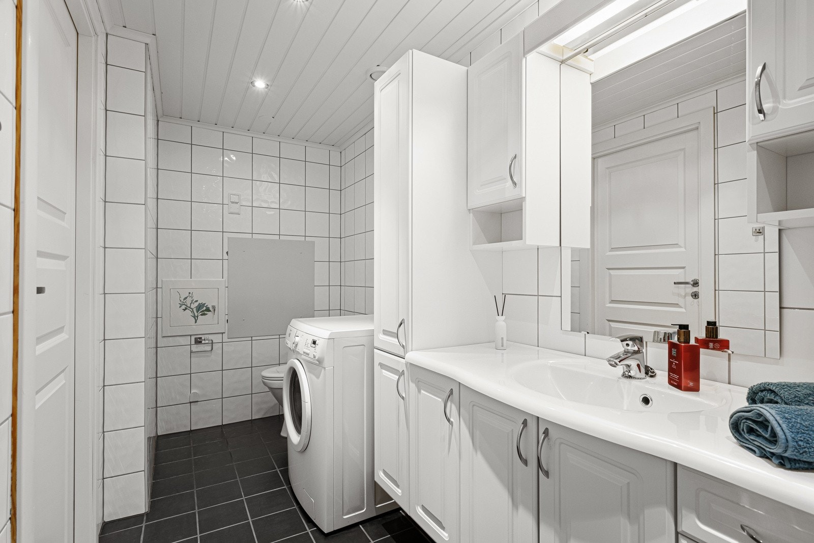 Badet har dusjkabinett, servant i romslig innredning, toalett og opplegg for vaskemaskin Galleribilde
