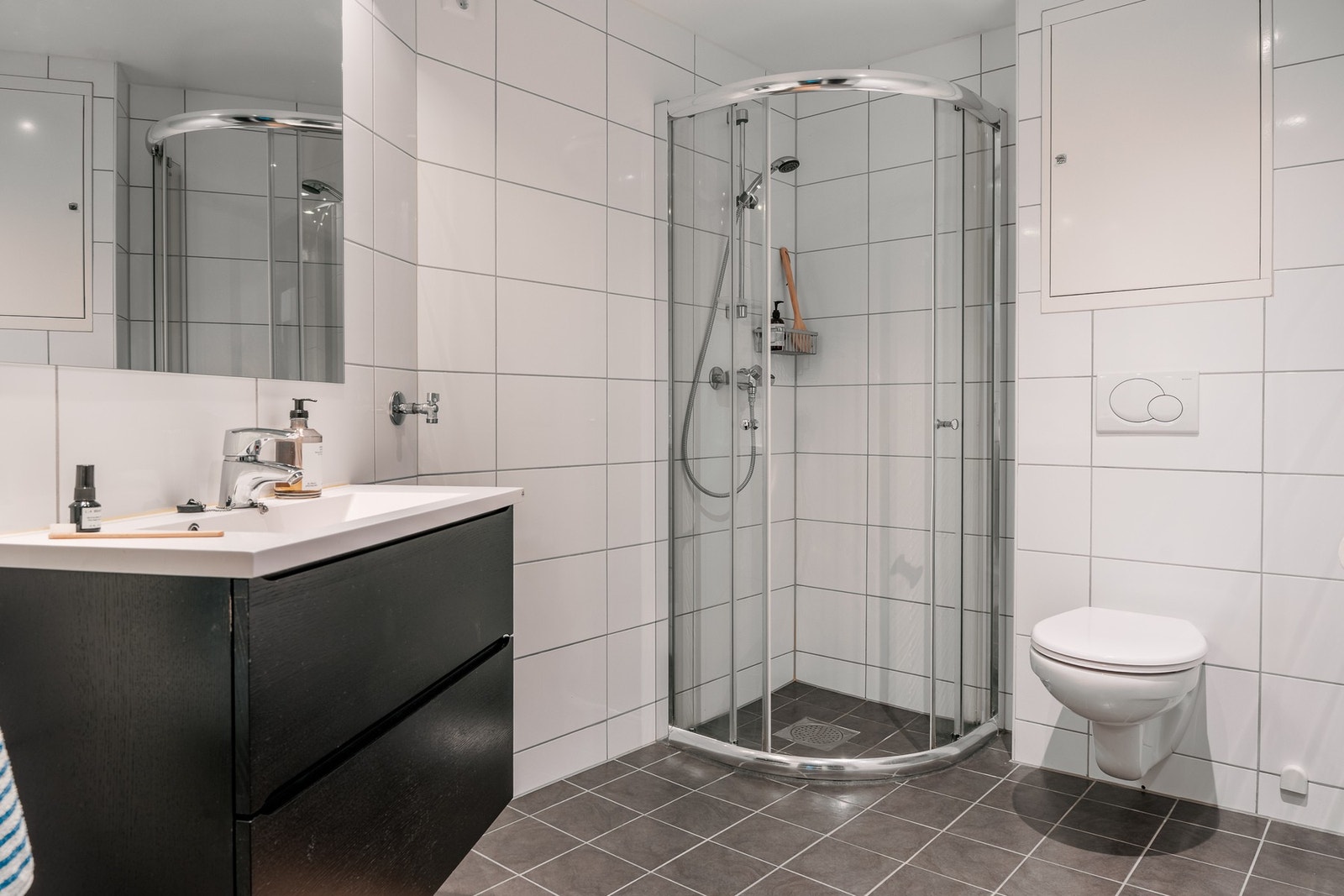 Badet er innredet med vegghengt toalett, dusjhjørne med glassvegger, og baderomsmøblement med speil og belysning. Galleribilde