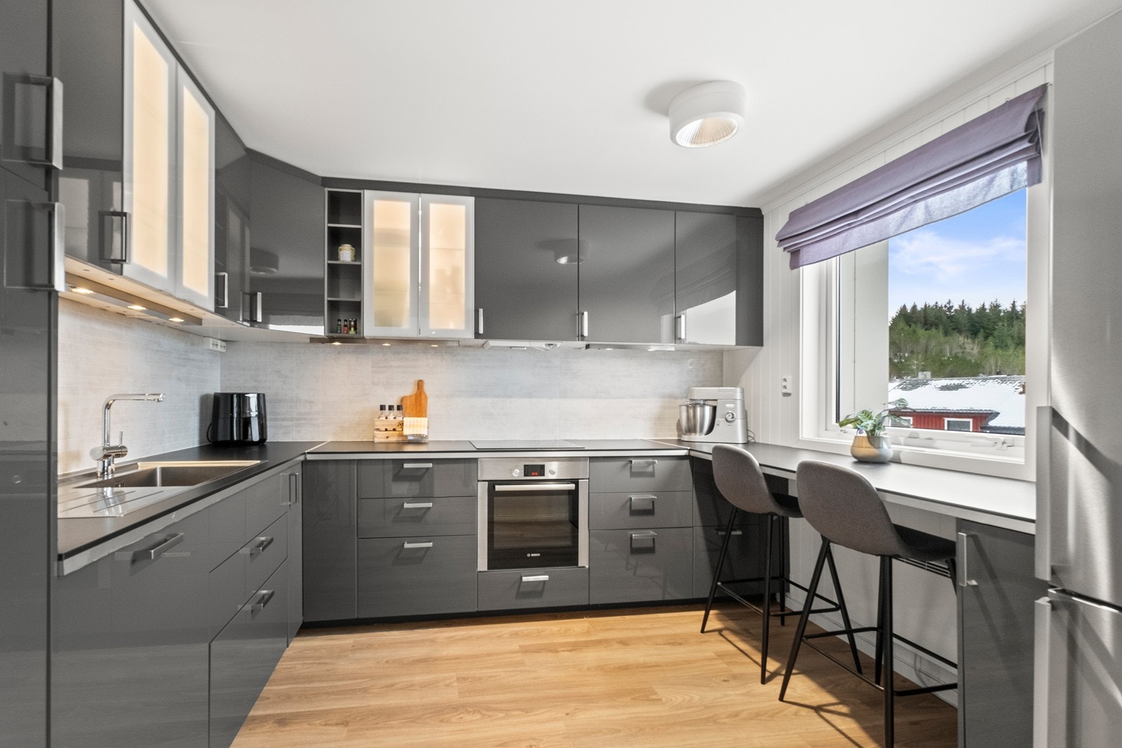 Stort kjøkken i grå høyglans med mye benkeplass og barløsning hvor man kan spise frokost og nyte utsikten! Galleribilde