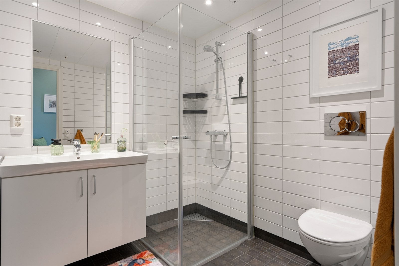 Badet er utstyrt med dusjhjørne, vegghengt toalett og en lys baderomsinnredning. Galleribilde
