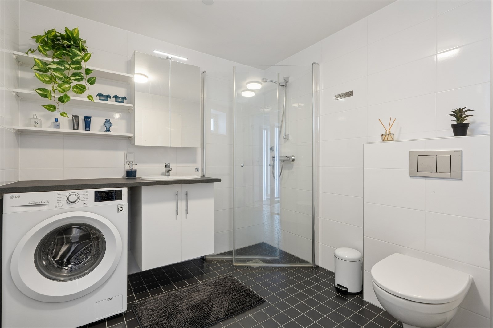 Badet er helfliset og har varmekabler i gulvet for ekstra komfort. Badet er ellers utstyrt med dusjhjørne, vegghengt toalett og baderomsinnredning med nedfelt servant. I tillegg har man opplegg for vaskemaskin. Galleribilde