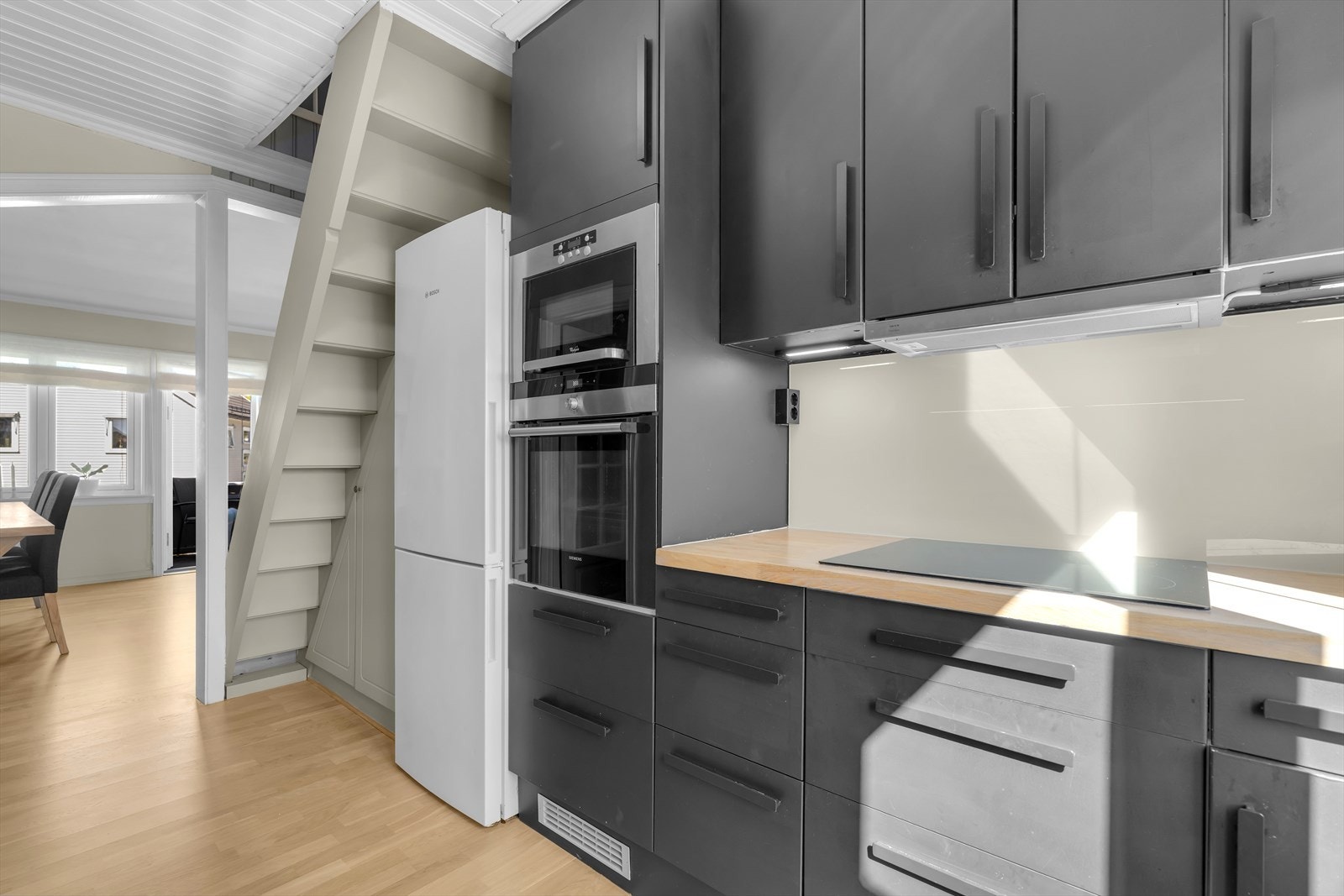 Kjøkkenet er gjennomtenkt og funksjonelt innredet, med stilrene, mørke fronter som gir et moderne uttrykk, samt en benkeplate i heltre. Galleribilde