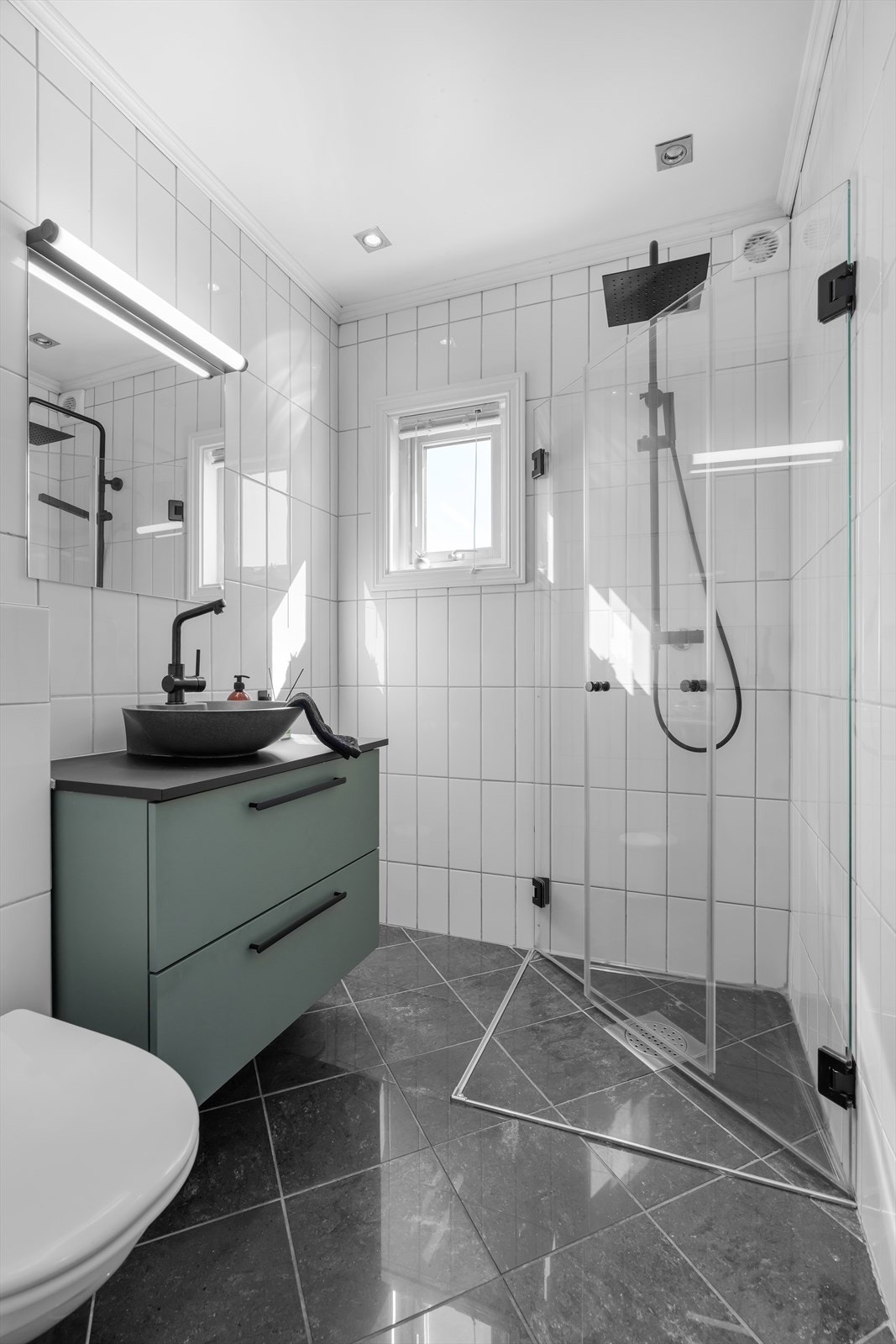 Badet har flislagt gulv med elektriske varmekabler. Innredningen med servant ble montert i 2022, og rommet har et vegghengt toalett og et dusjhjørne med glassdører. Galleribilde