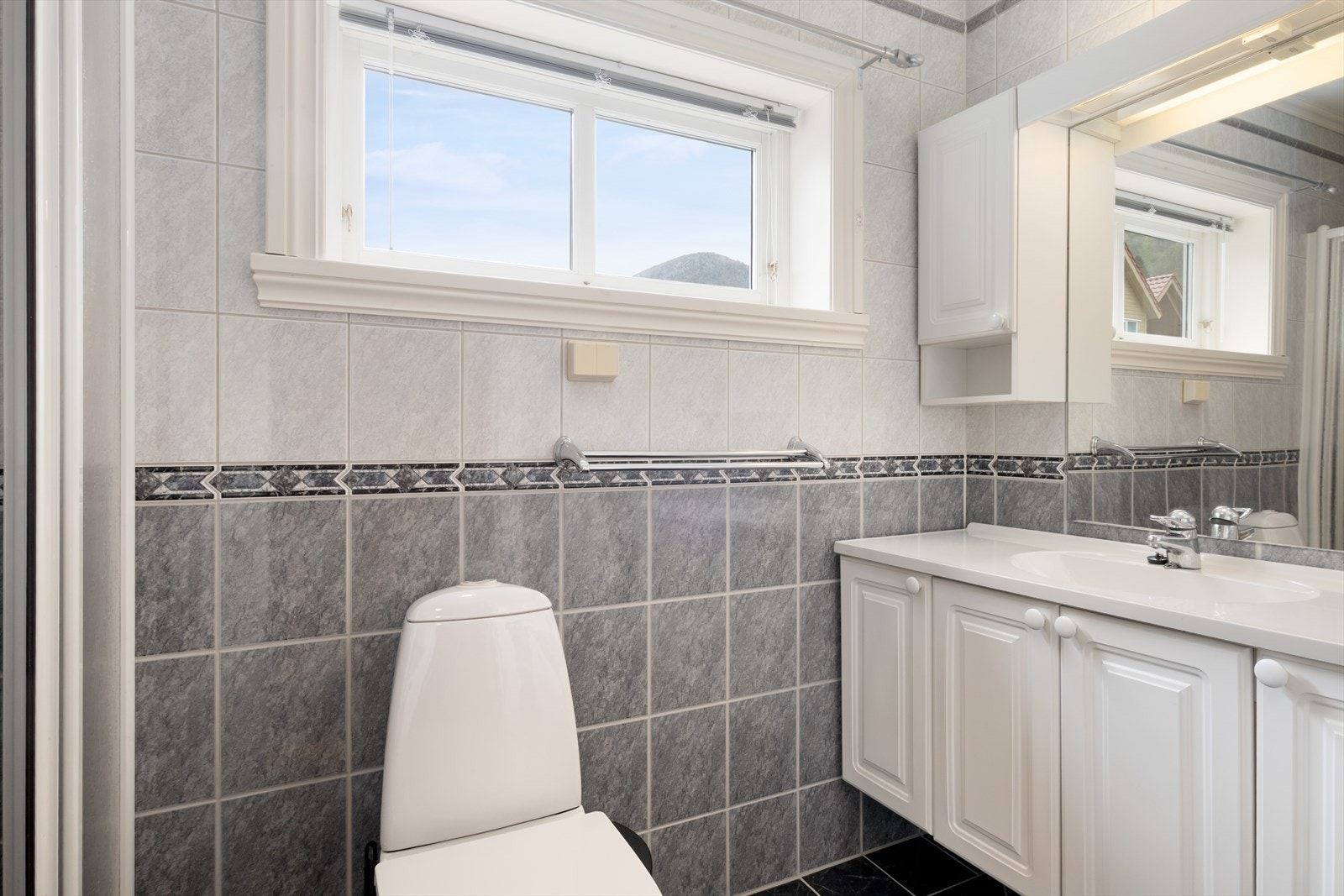 Bad frå 2001 med flisar på golv og veggar. Badet inneheld dusjnisje med skyvedør, golvmontert toalett og servantskao med heilstøypt servant, overskap, speigel og lyslist. Galleribilde