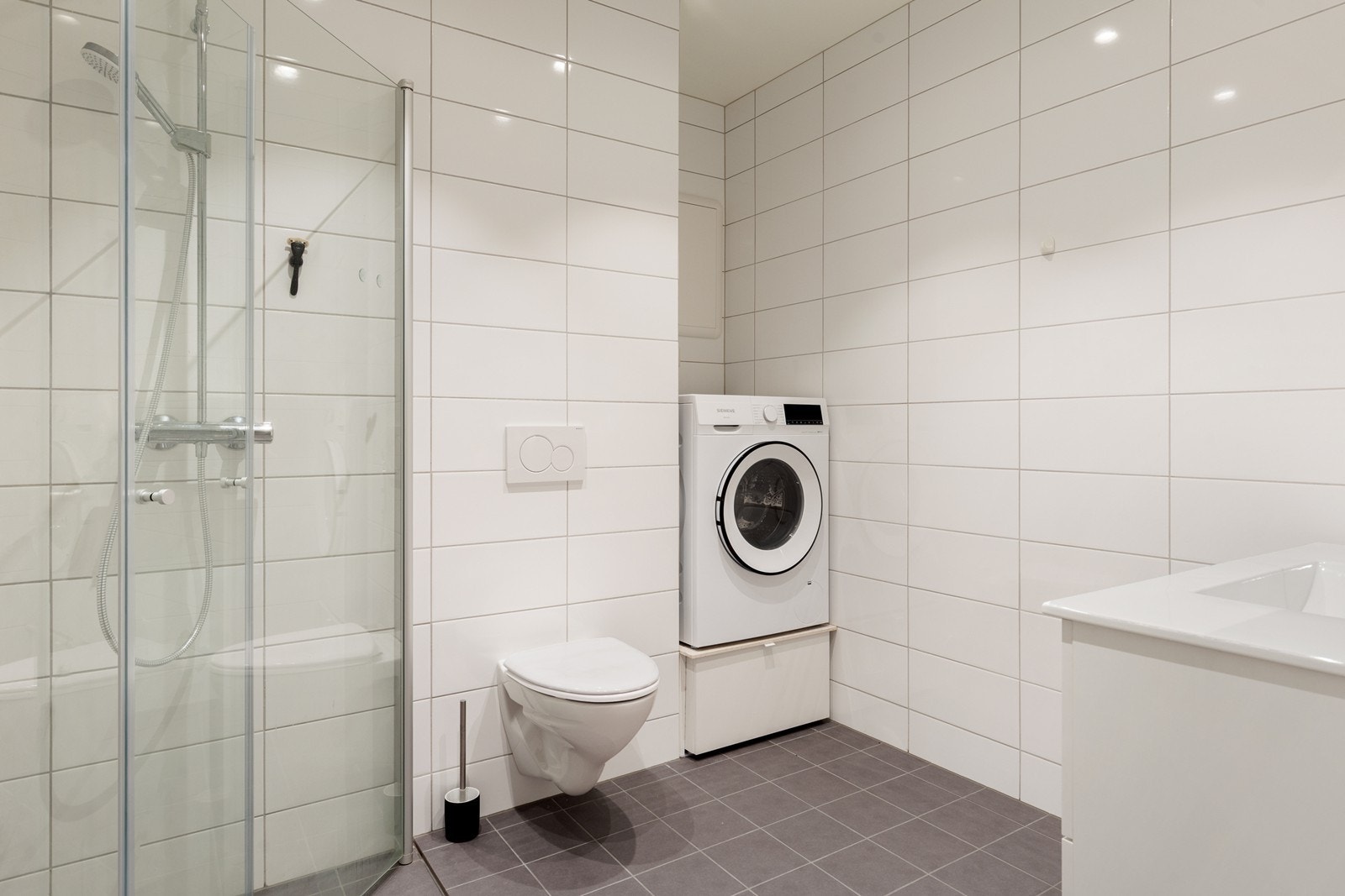 Badet er utstyrt med dusjvegger, vegghengt toalett og opplegg for vaskemaskin. Galleribilde