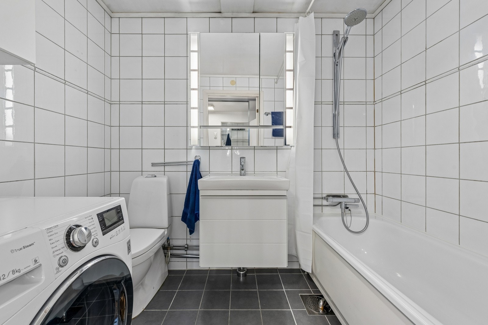 Baderom med toalett, servant med skuff under og dusj i badekar. Det er også opplegg til vaskemaskin på badet. Galleribilde