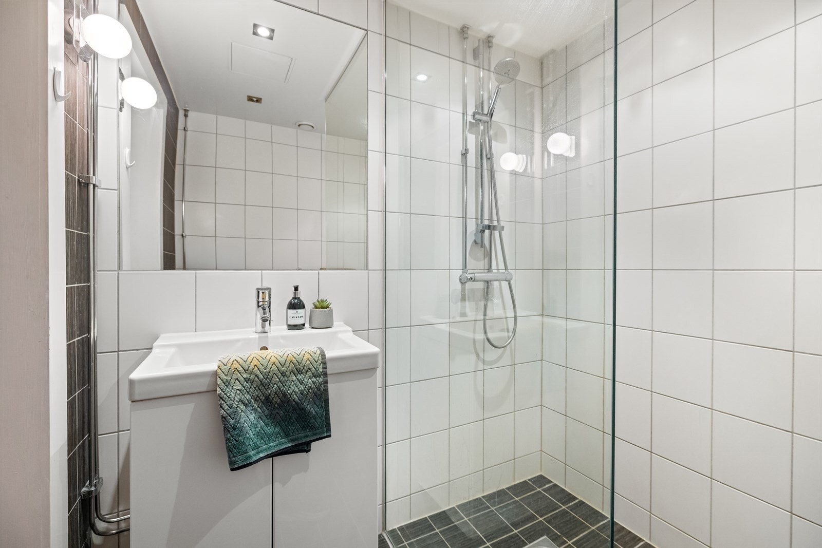 Badet er utstyrt med servantskap med glatte, folierte fronter og heldekkende servant, samt speil med lysarmatur over servant. Galleribilde
