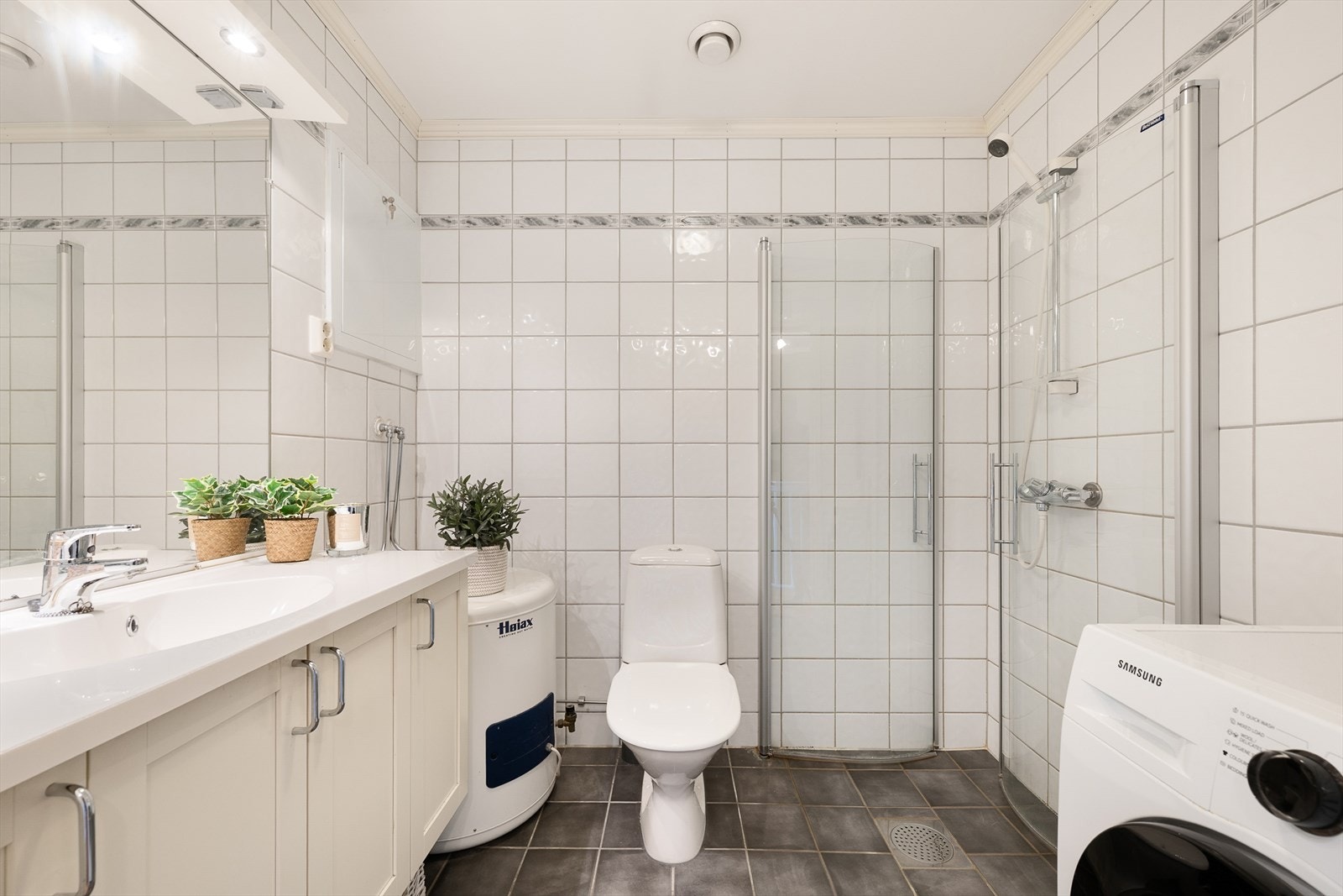 Badet har flislagt gulv med gulvvarme, dusjdører i herdet glass, WC og opplegg for vaskemaskin. Galleribilde