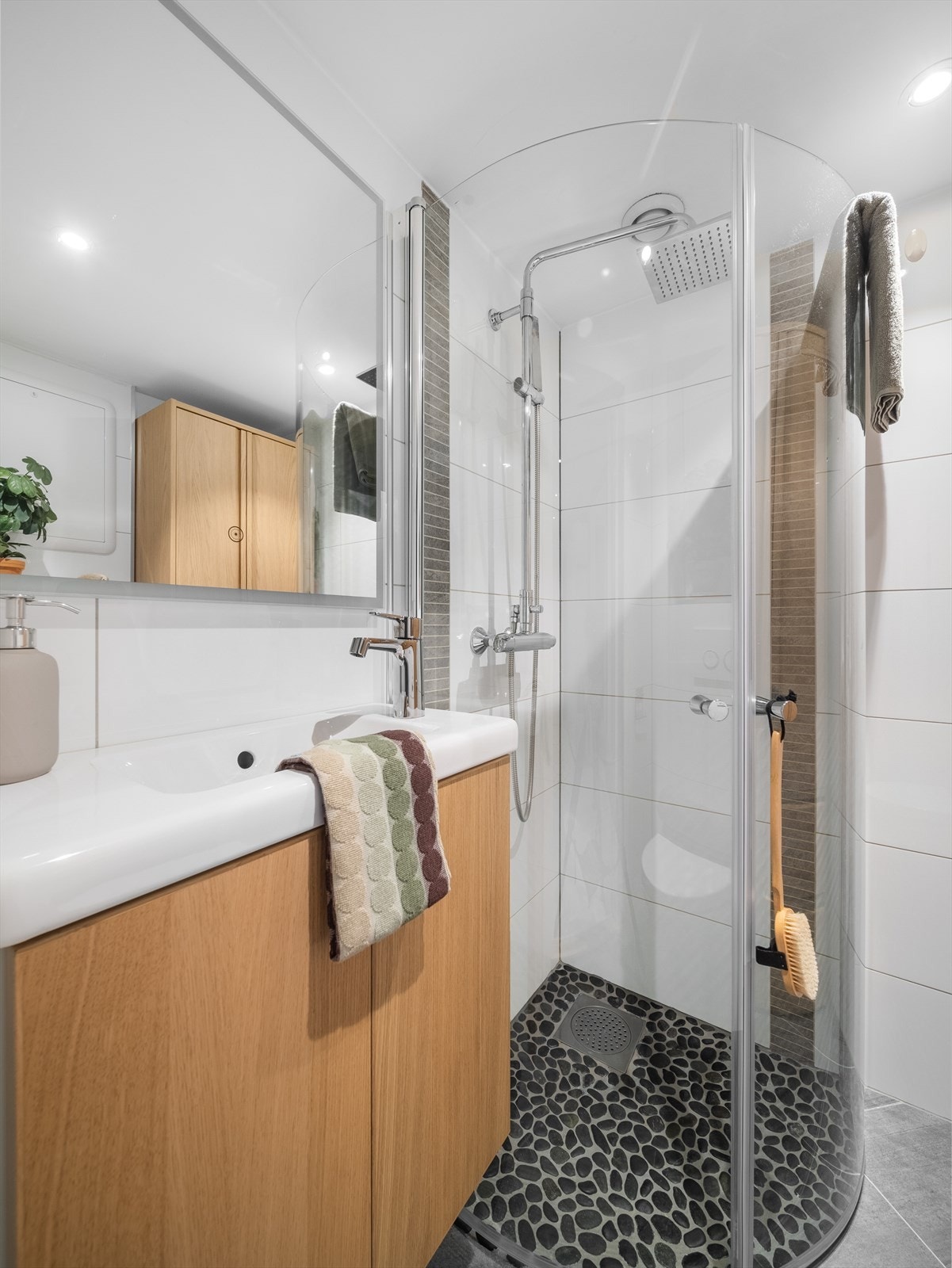 Badet er innredet med innfellbart dusjhjørne i glass, vegghengt toalett med innebygd sisterne og servant med moderne baderomsinnredning og speil med integrert belysning. Galleribilde