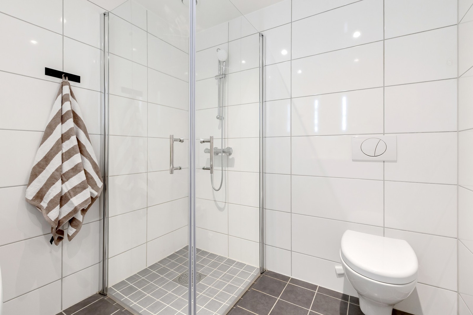 Badet er utstyrt med dusjhjørne, servant med underskap, speil med integrert lys og opplegg for vaskemaskin Galleribilde