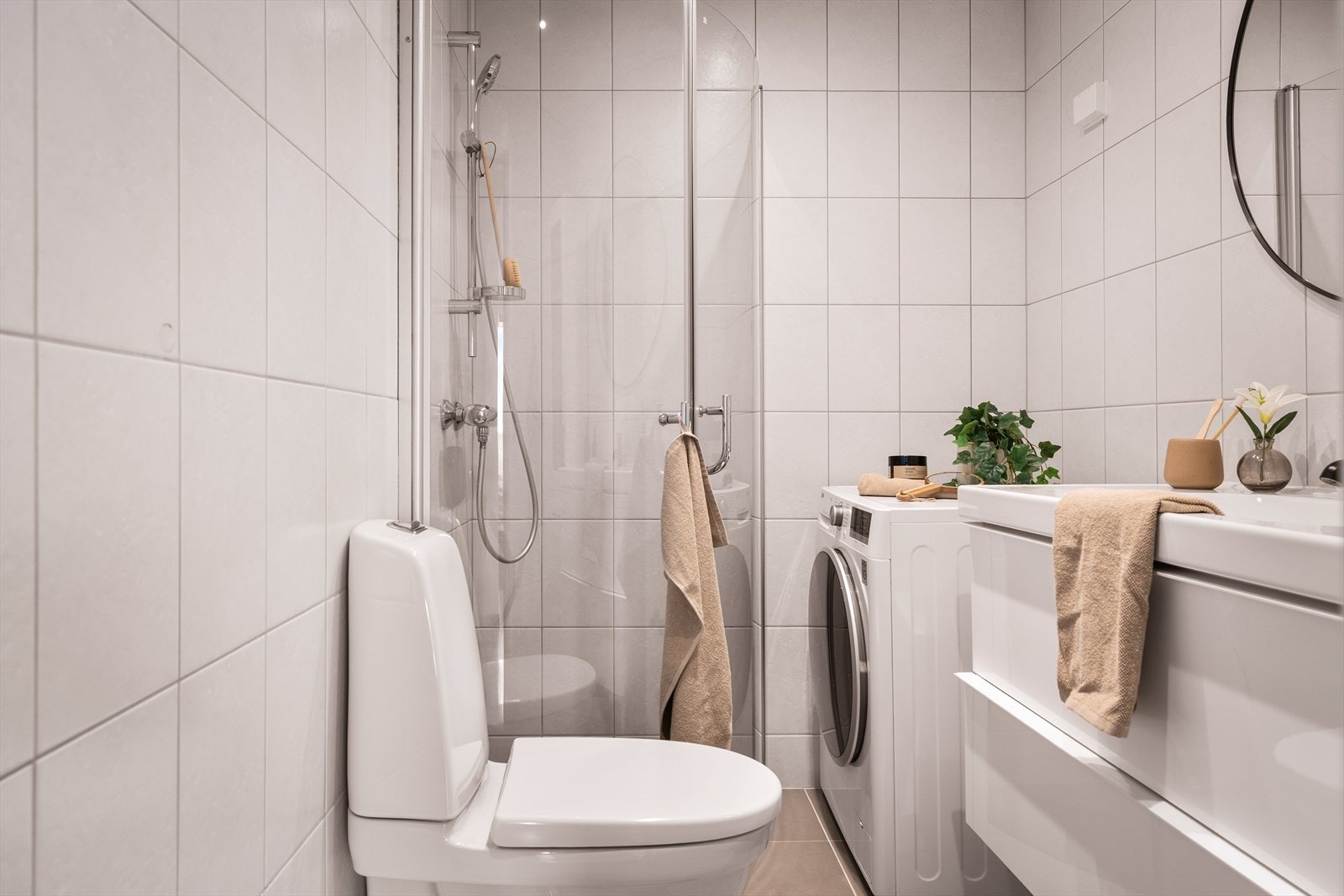 Flott helfliset bad med varmekabler i gulv. Badet er utstyrt med innfellbart dusjhjørne av glass, klosett og møblement med servant. Det er speil og vegghengt smalt skap. Opplegg for vaskemaskin. Galleribilde