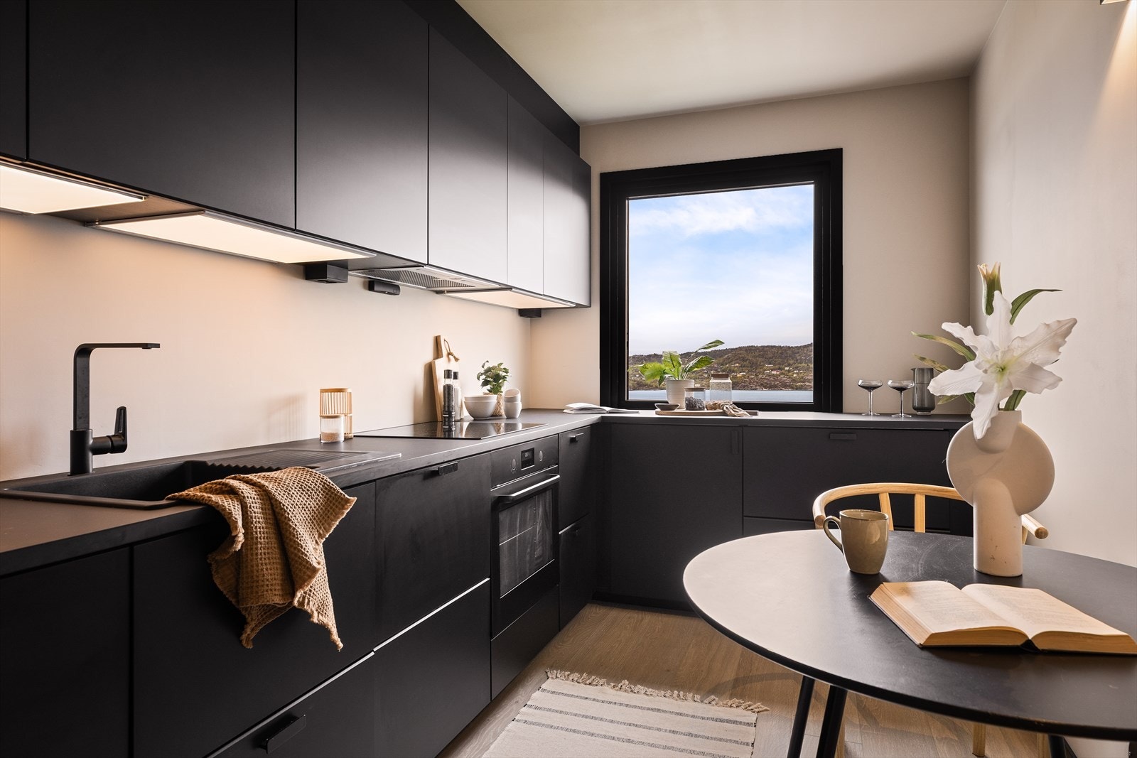 Kjøkkeninnredning i sort slett utførelse med takhøye skap og grå/mørk laminat benkeplate. Det er lys og strømuttak under overskap. Galleribilde
