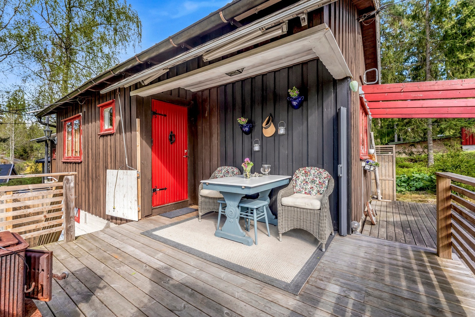 Uteområde med terrasse og inngangsparti, malt i mørke farger med kontrasterende røde detaljer. Galleribilde