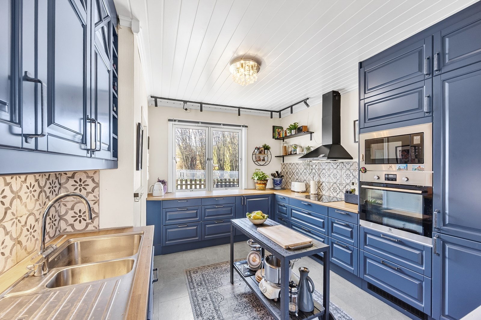 Kjøkkeninnredningen har blå, profilerte fronter og laminert benkeplate. Det er lagt dekorfliser på vegg over benkeplaten. Galleribilde