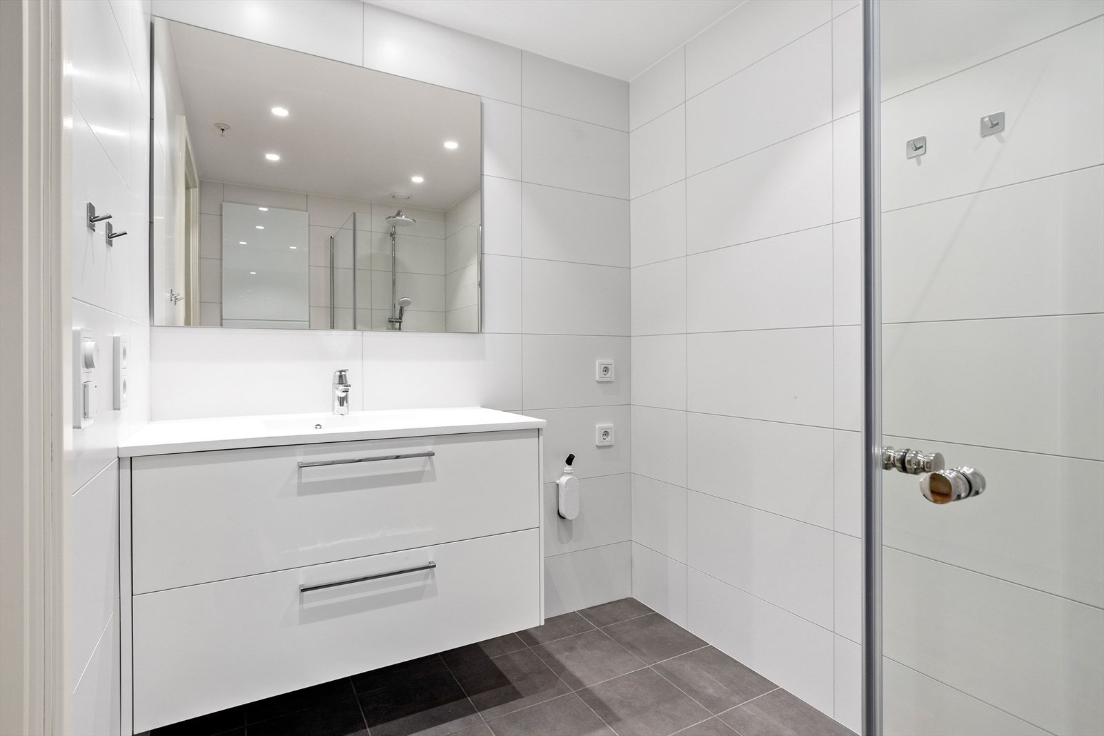 Baderomsinnredningen består av servant, skuffer under servant, speil, innfellbare glassvegger til dusjen og vegghengt toalett fra Grohe. Det er tilrettelagt for både vaskemaskin og tørketrommel, og badet har praktiske LED-downlights. Galleribilde