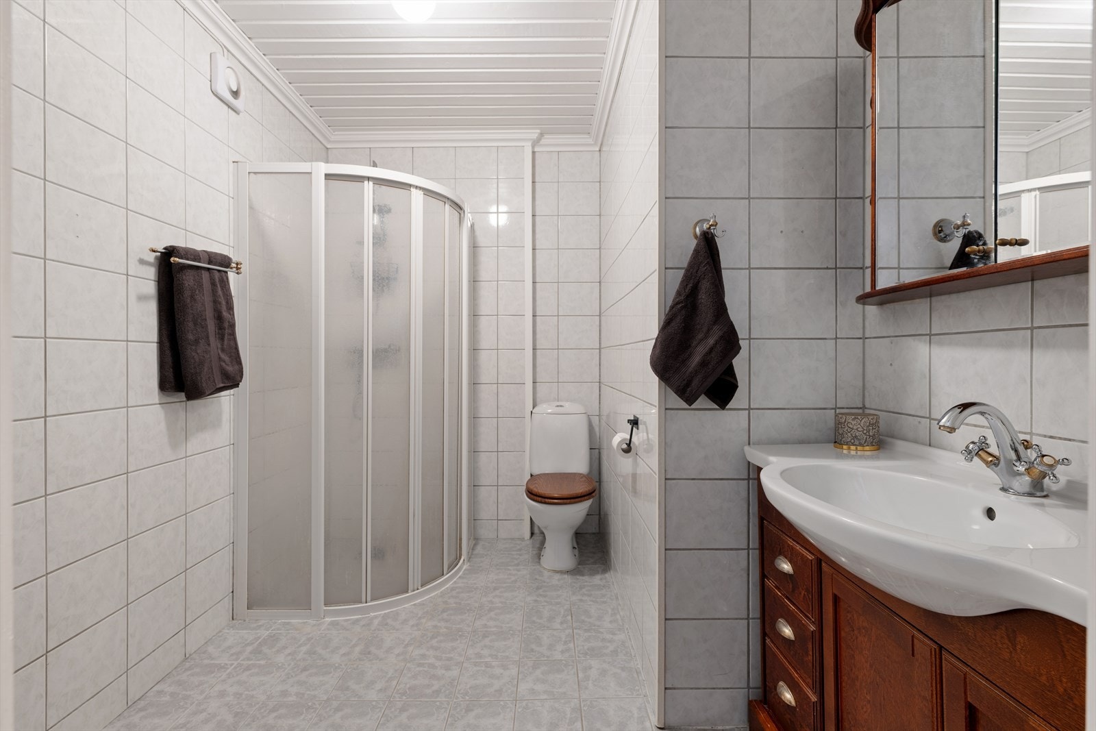 Badet er innredet med dusjhjørne, toalett, romslig servantinnredning med skuffer og skap og matchende speilskap med integrert lys Galleribilde