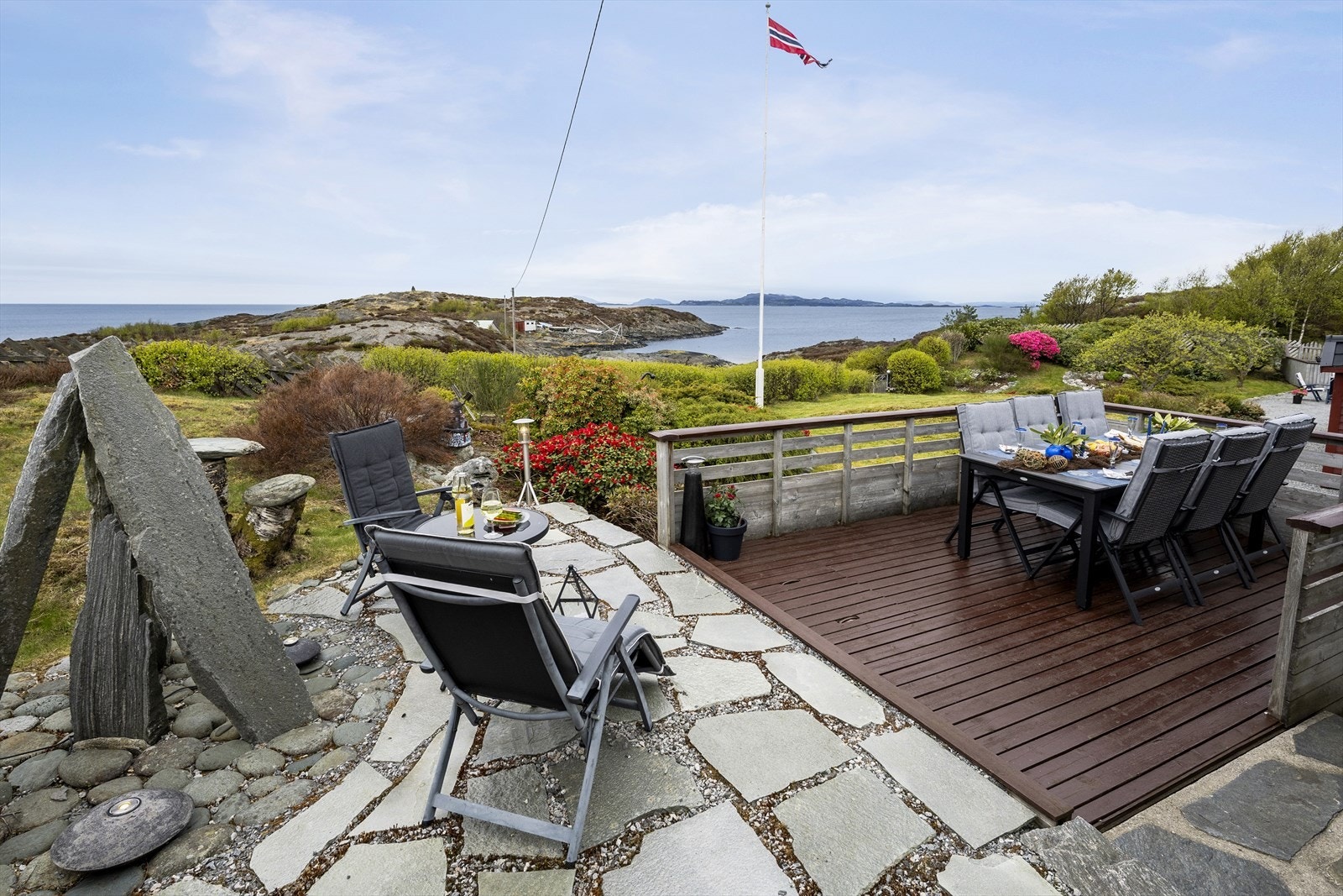 Kombinasjonen av treterrasse og hellelagd uteplass skaper variasjon i hagen. Legg merke til den plassbygde kunsten til venstre. Galleribilde