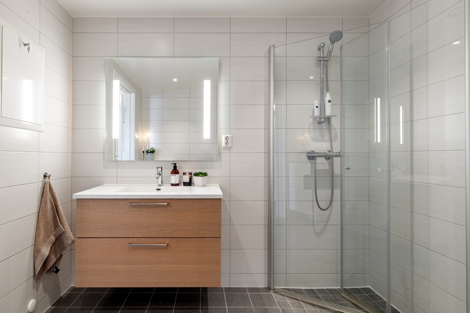 Badet er innredet med servantskap med heldekkende servant og speil med belysning. Videre har badet en stilren dusjløsning med glassvegger samt vegghengt toalett. Galleribilde