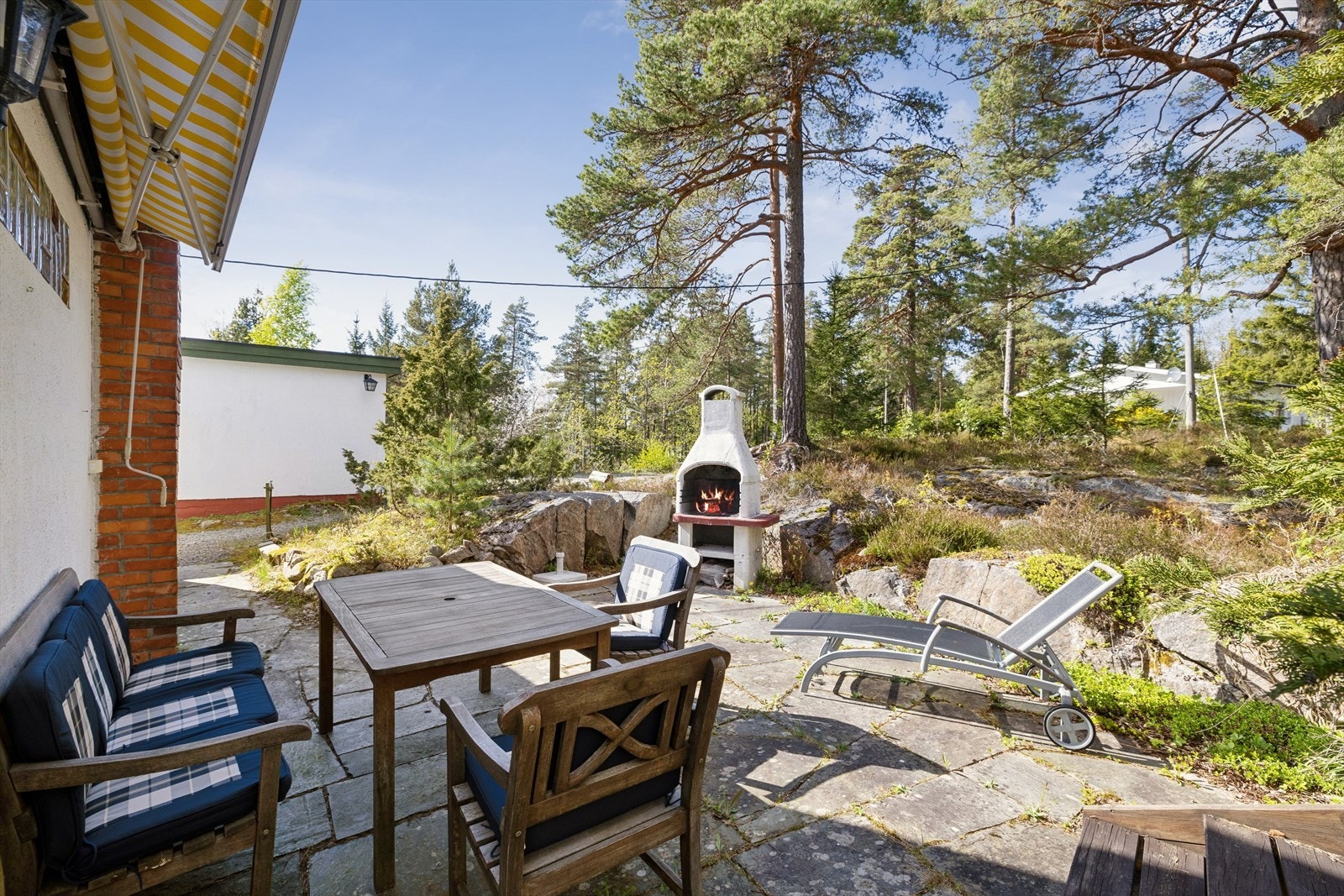 Ved inngangssiden av hytta finner du en skiferbelagt uteplass med utepeis, omkranset av naturtomt. Galleribilde