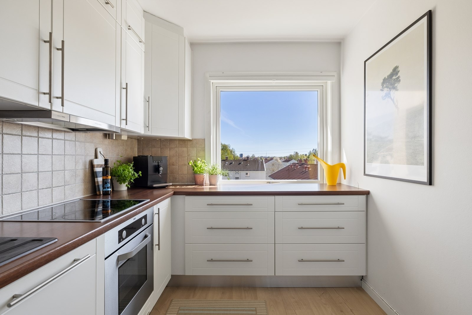 Kjøkkenet består av en innredning med glatte fabrikklakkerte fronter, laminat benkeplate med nedfelt lum i kompositt/plast, downlights under overskap, og fliser på vegg over benkeplaten. Galleribilde
