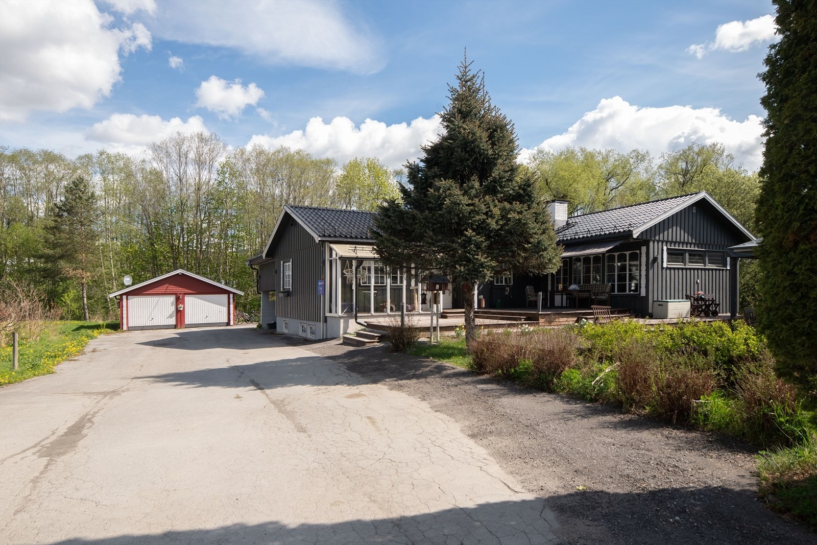 Stor, asfaltert gårdsplass med biloppstillingsplasser og carport, samt dobbeltgarasje med vippeporter og ladepunkt for elbil. Galleribilde