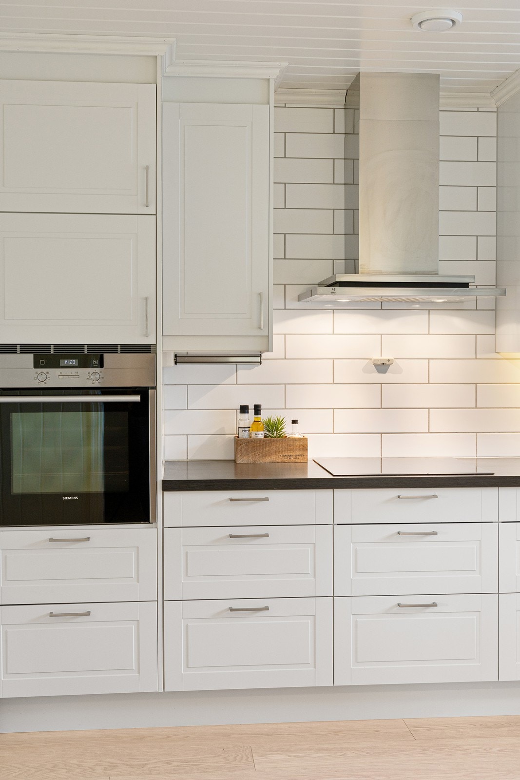 Kjøkkeninnredningen har hvite profilerte fronter og laminert benkeplate. Det er fliser på vegg bak ventilatoren og over benkeplaten. Galleribilde