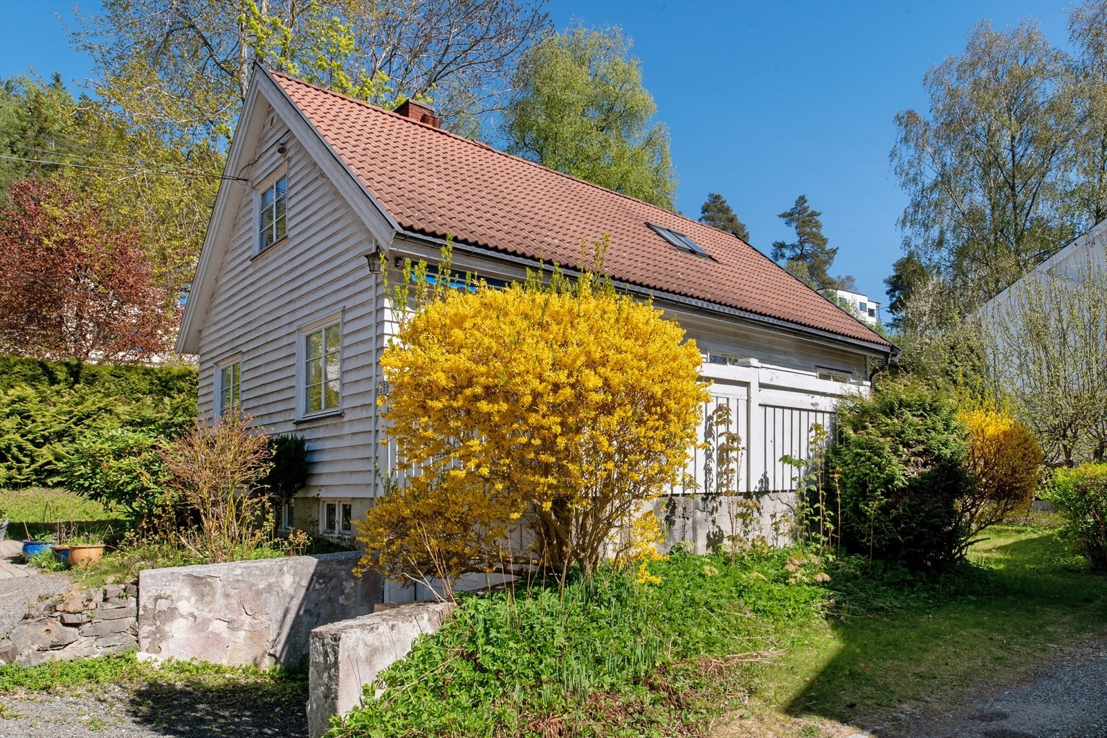 Tomten er opparbeidet med gruslagte flater, brostein, gressplen og variert beplantning, og ligger i et svakt skrånende terreng. Galleribilde