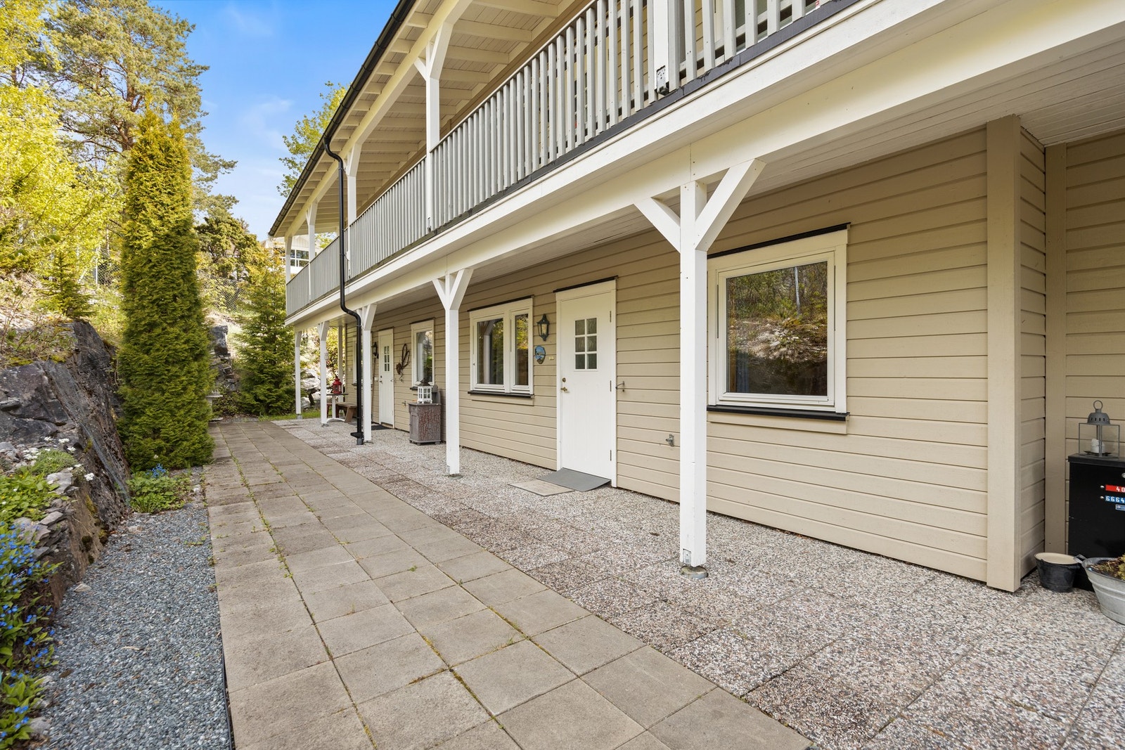 Inngangsparti med steinheller. Det er pent beplantet med busker og blomster. Galleribilde