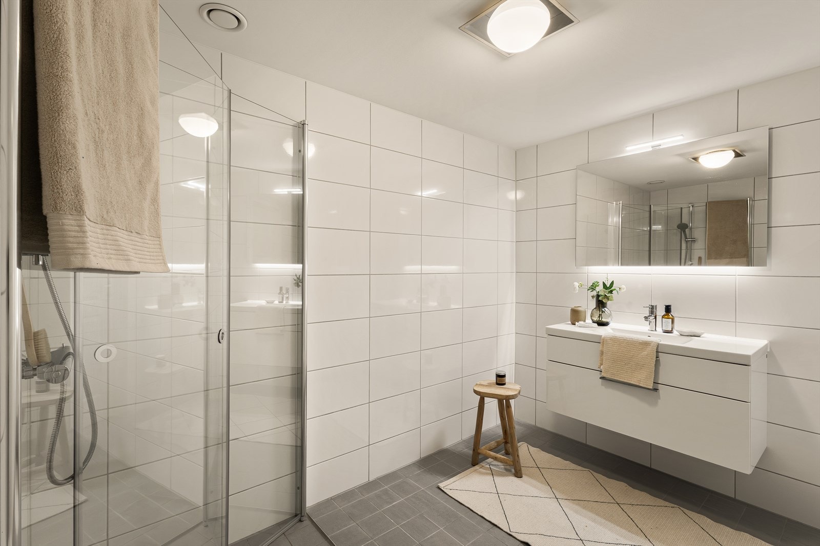 Flott helfliset bad med innfelte spotlights i himling og varmekabler i gulv. Badet er utstyrt med servant med møblement/speil, belysning, vegghengt toalett, dusjgarnityr og innfellbart dusjhjørne. Galleribilde