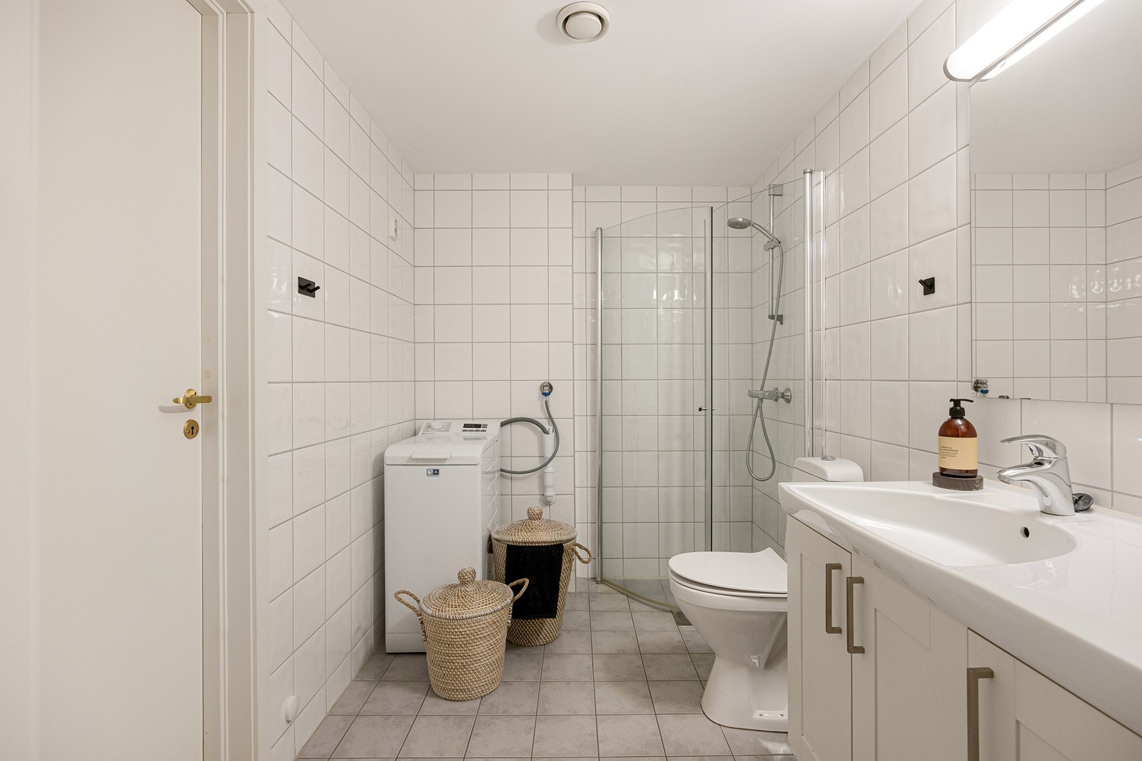 Badet er helfliset og har lun gulvvarme. Videre er toalettet er gulvmontert, dusjhjørnet har innfellbare glassdører og det er opplegg for vaskemaskin. Galleribilde