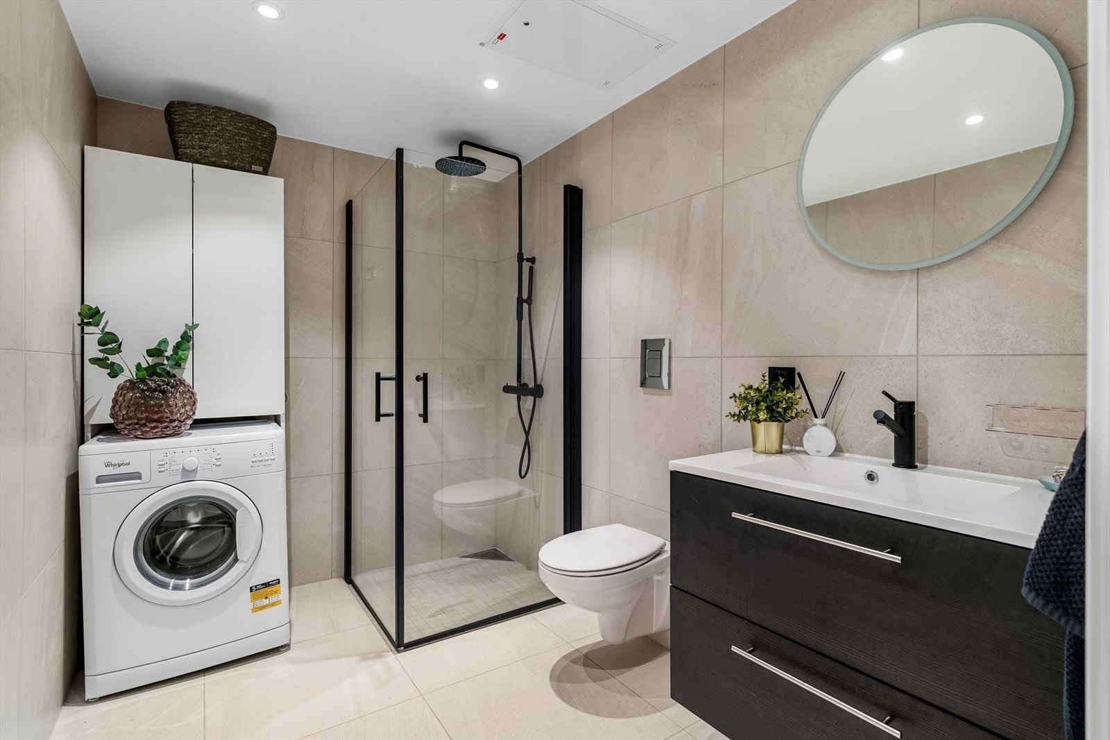 Badet har gulvvarme, downlights i taket og balansert ventilasjon. Innredningen består av servantskap med oppbevaring, speilskap, dusjhjørne med sorte detaljer, vegghengt toalett og opplegg for vaskemaskin. Galleribilde