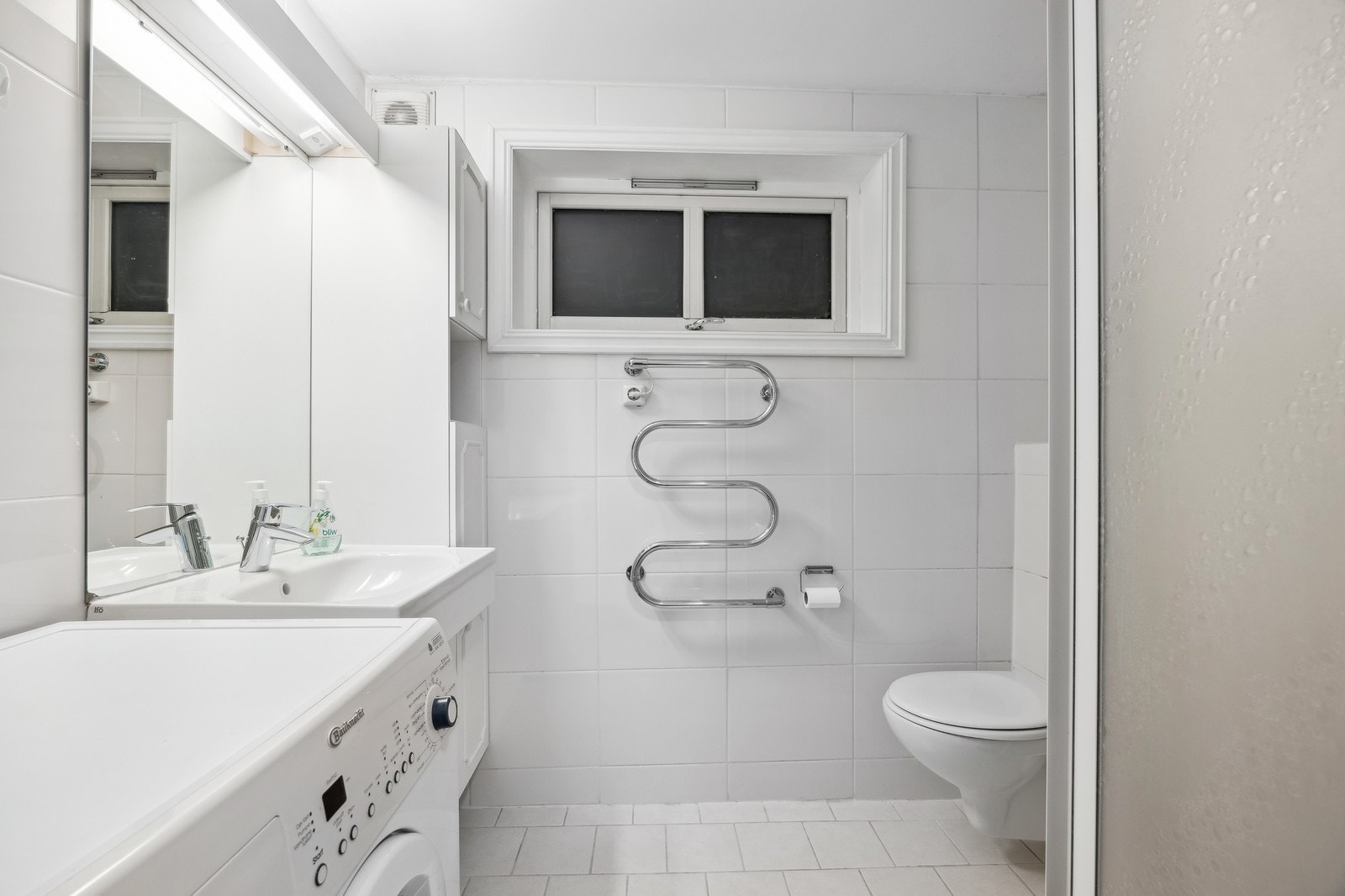 Bad med vaskemaskin, servant, baderomsinnredning og dusj. Det er varmekabel i gulvet. Galleribilde