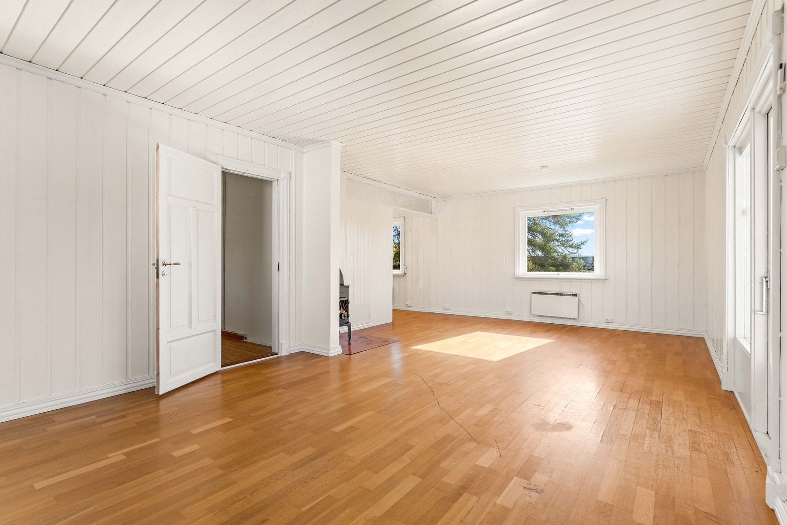 Romslig stue med parkettgulv, panel på veggene og plass til flere møbelgrupper. Galleribilde
