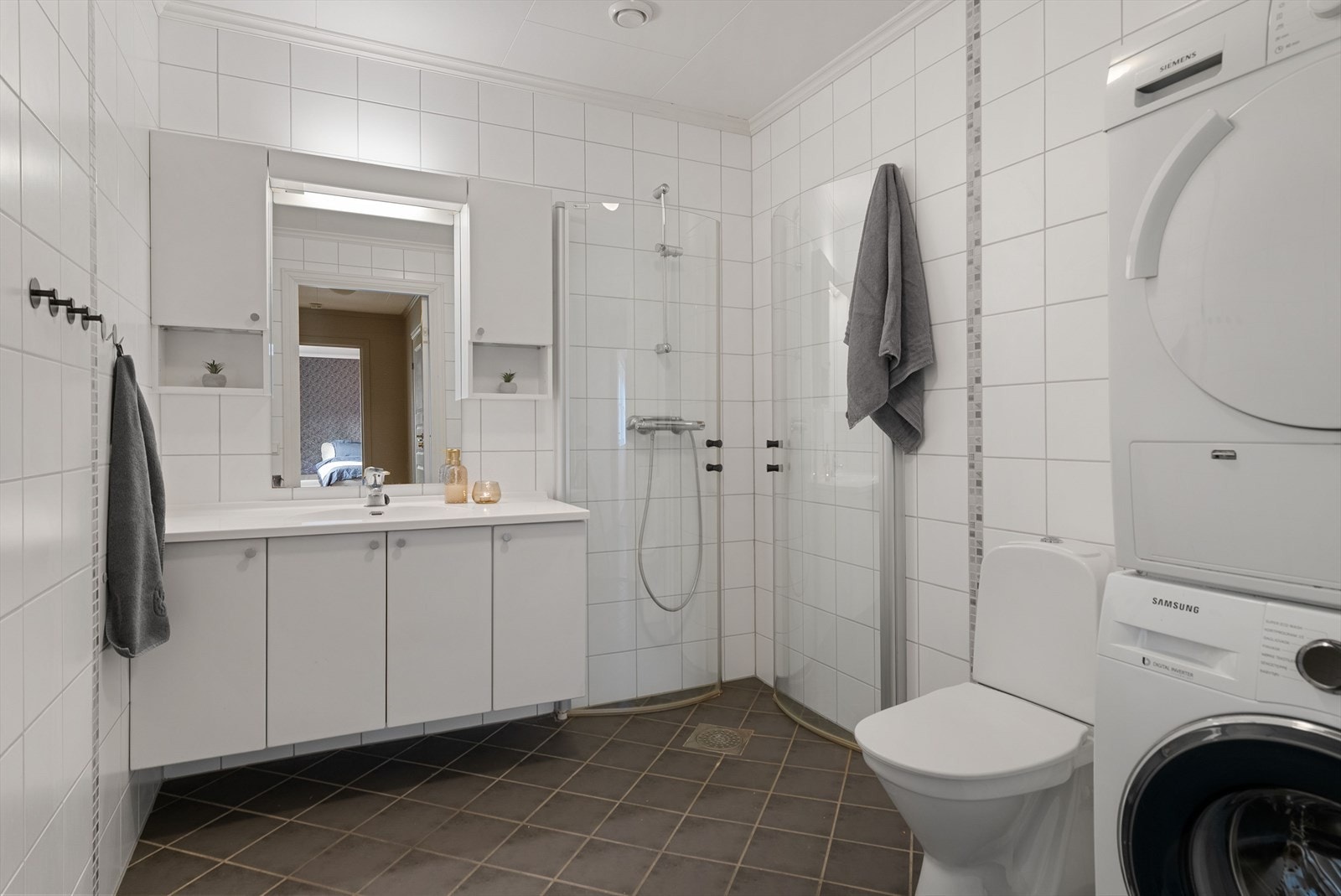 Flislagt bad med dusjhjørne med innfellbare glassvegger, toalett, servantinnredning og opplegg for vaskemaskin. Galleribilde