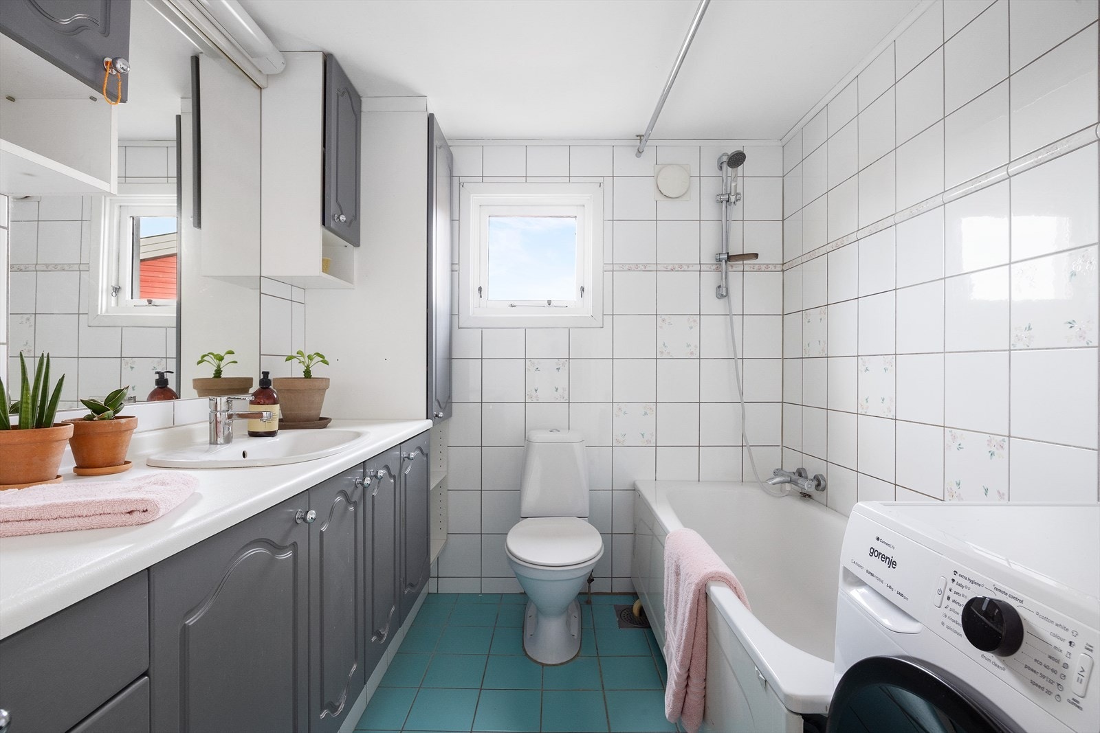 Badet har flislagte gulv og vegger samt malt himling. Rommet er innredet med servantskap med malte, profilerte fronter, laminat benkeplate, nedfelt servant med ettgreps armatur, badekar, opplegg for vaskemaskin og gulvstående wc. Galleribilde